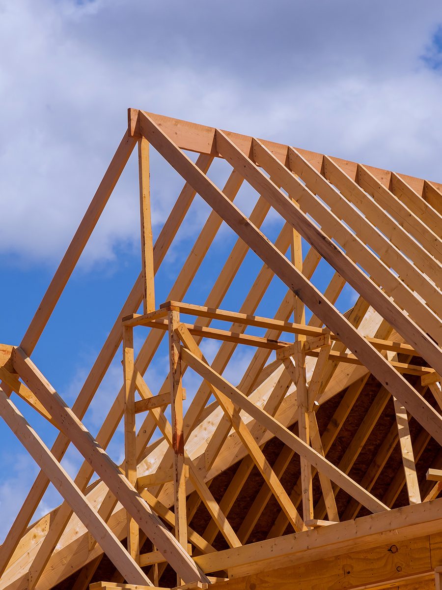 Wooden framework of a house under construction with a blue sky and clouds in the background.
