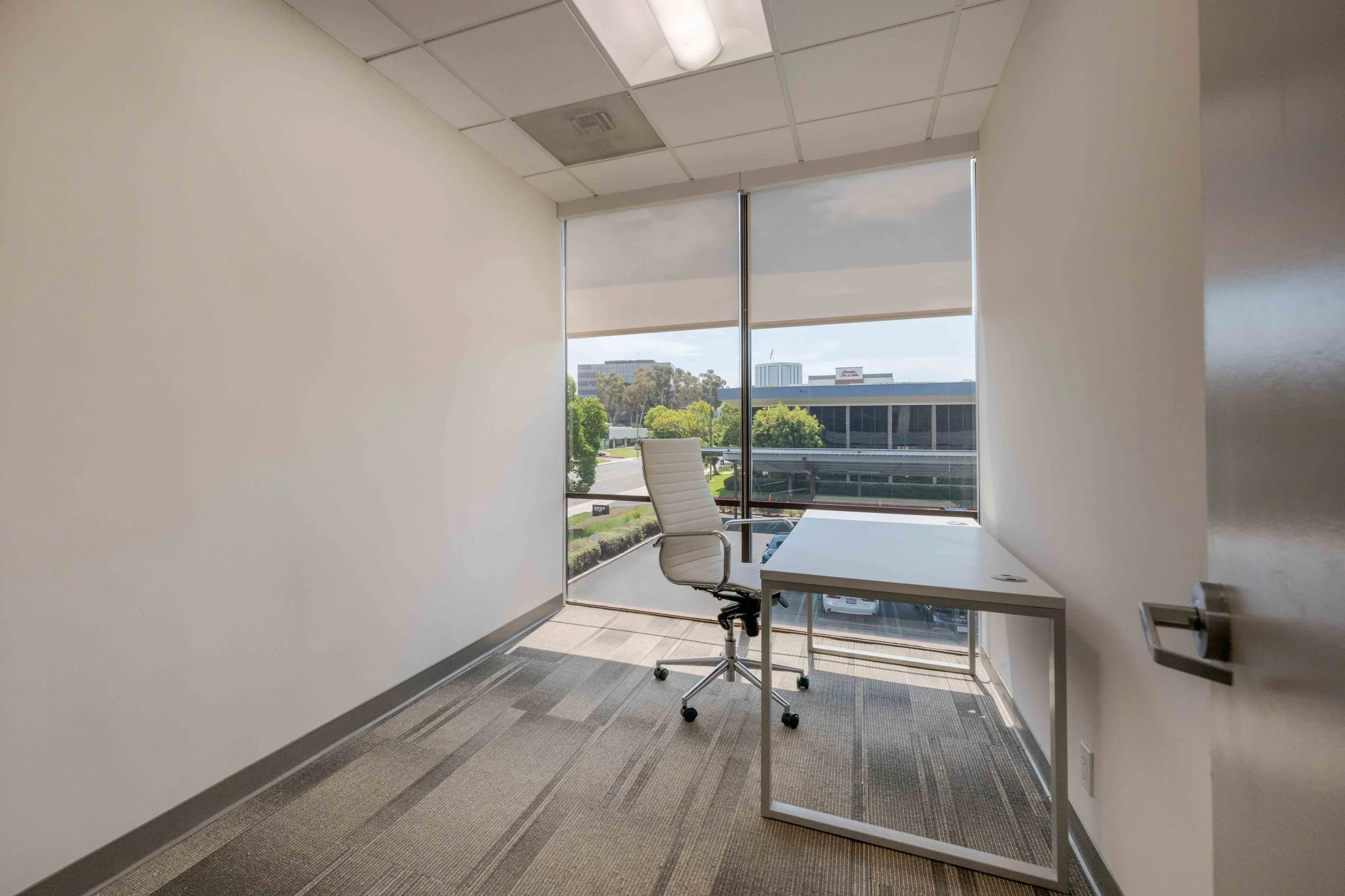 Private office with a desk and chair with floor to ceiling window at the back.