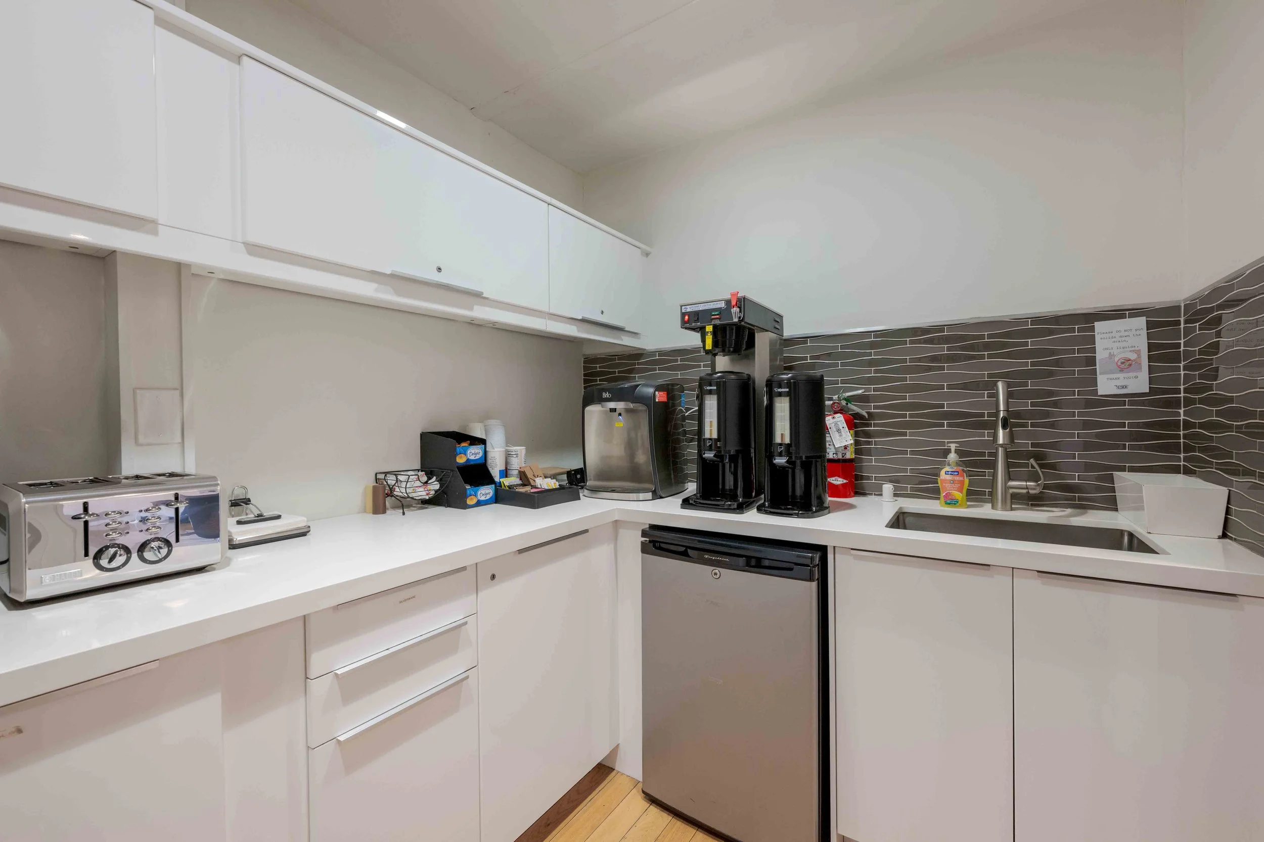 Office kitchen with a sink, toaster, coffee maker and storage.