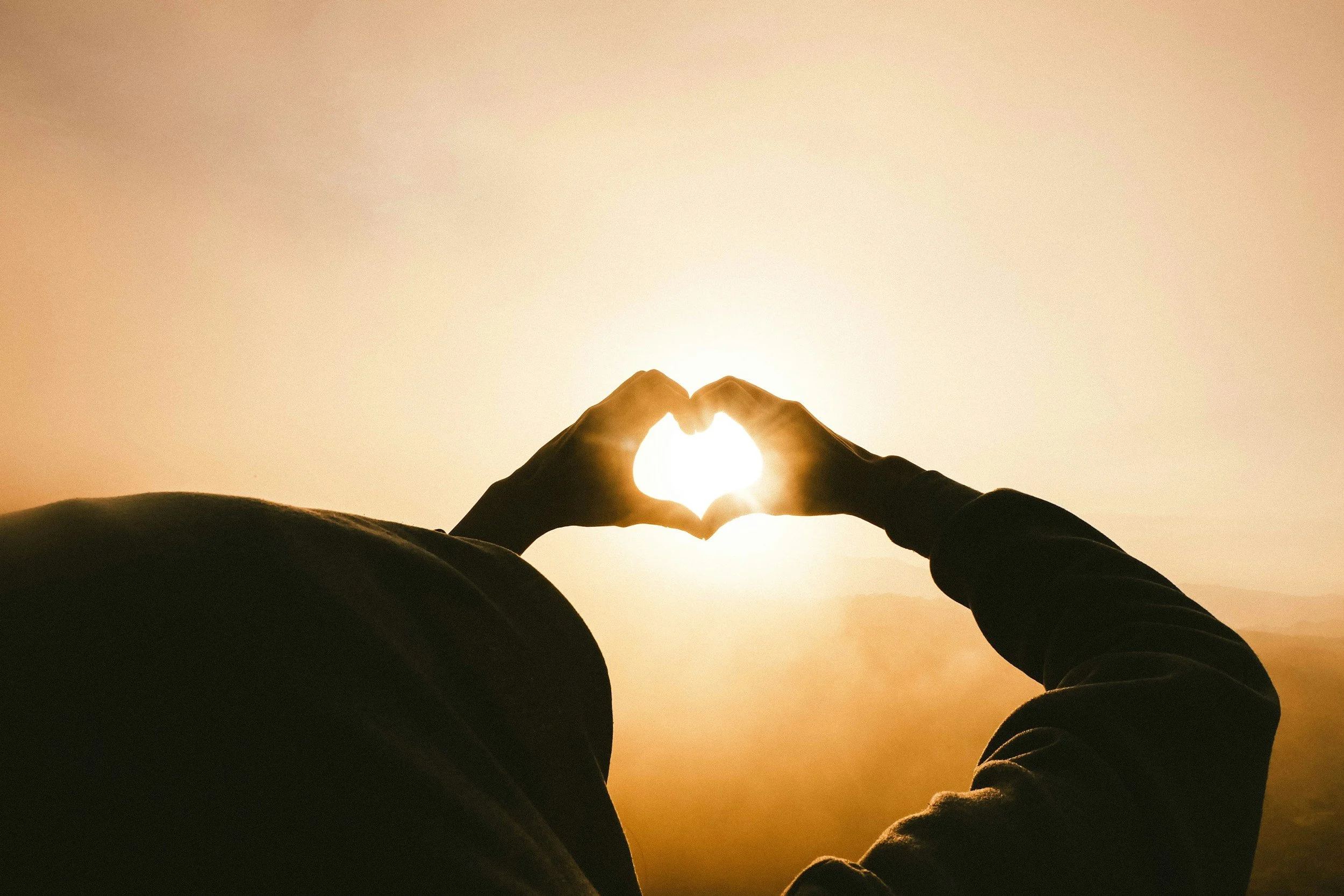 person making a heart shape with hands and holding it up to the sun