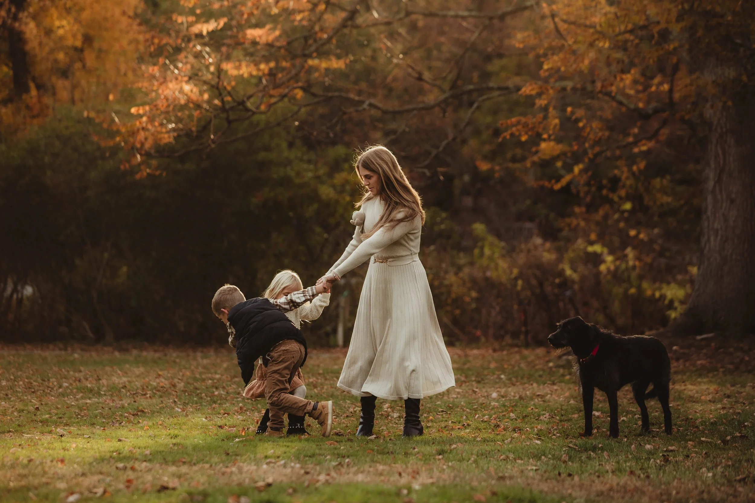 Steph and her two kids playing ring around the Rosie in a park with their dog next to them.