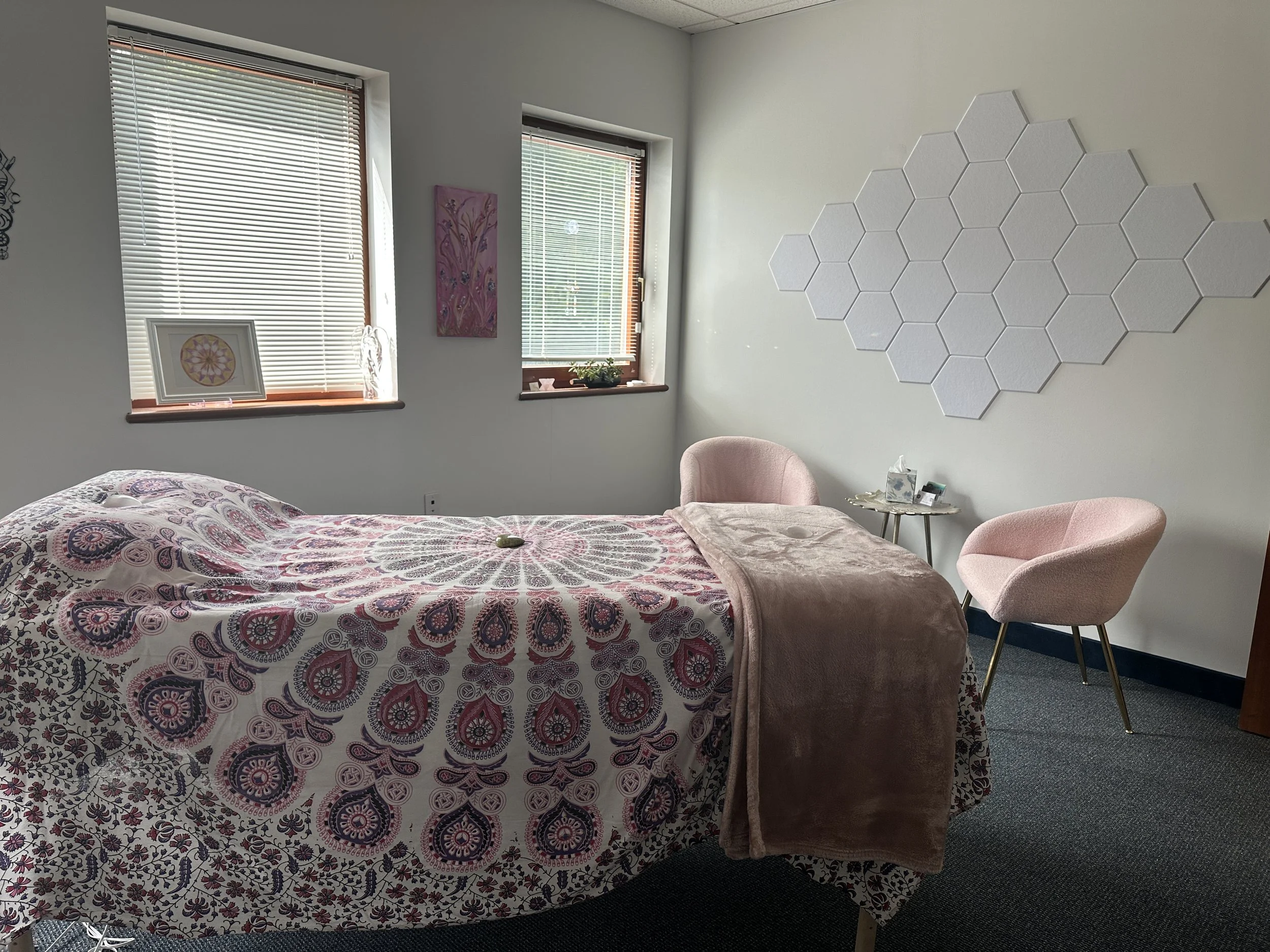 Image of a message bed with pink mandala sheets and blanket in a room with 2 pink chairs