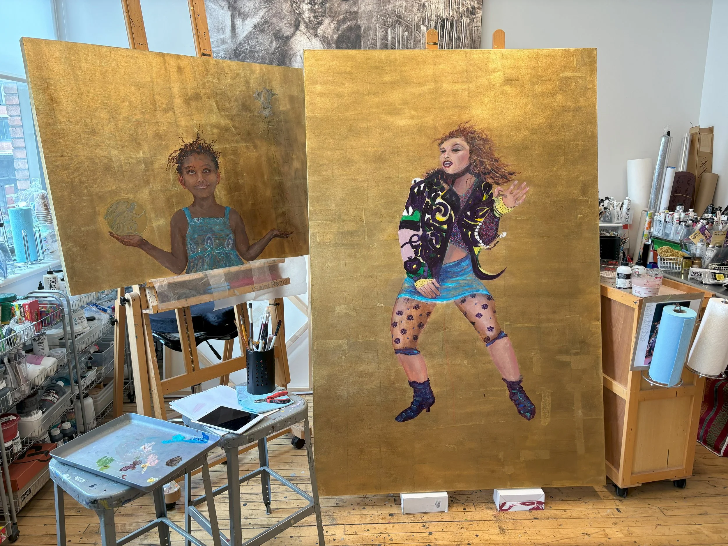 Two large paintings on easels in an art studio. The left painting depicts a young girl with curly hair holding a coin in each hand against a golden background. The right painting shows a woman with curly hair in a colorful outfit, performing on stage with a golden background. The studio has art supplies and a window in the background.