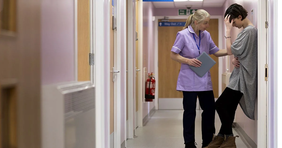 A nurse comforts a young woman who appears distressed in a hospital corridor.