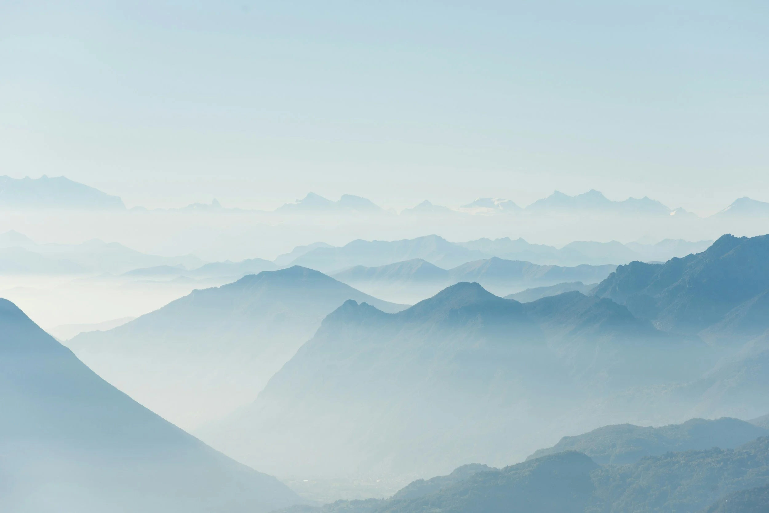 A scenic mountain landscape with multiple layers of mountain ridges fading into the distance under a clear sky.