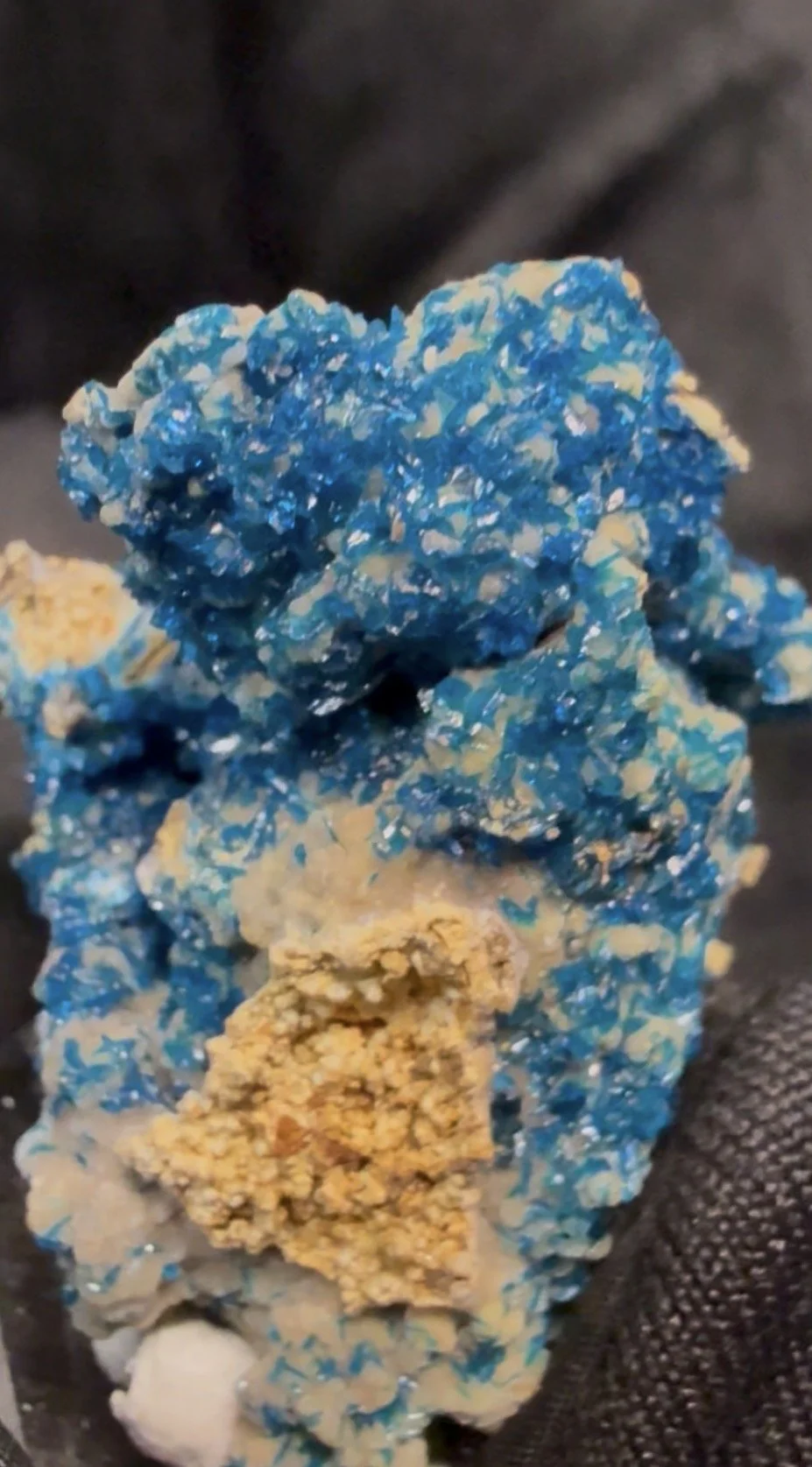Close-up of a Veszelyite mineral or crystal formation with blue and beige colors against a dark background.