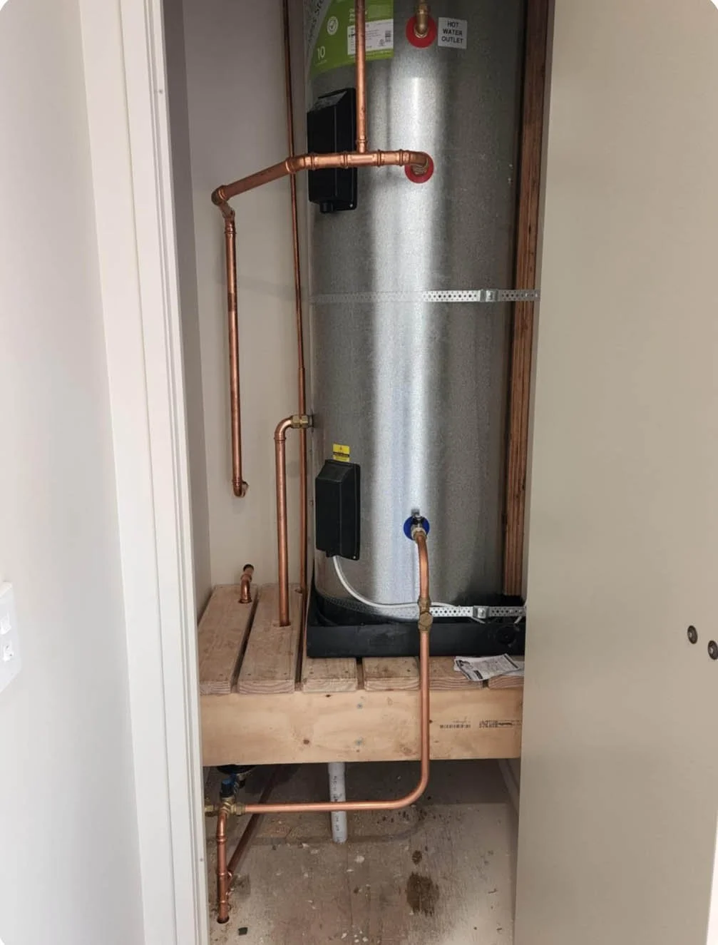 Water heater with exposed copper plumbing in a utility closet.