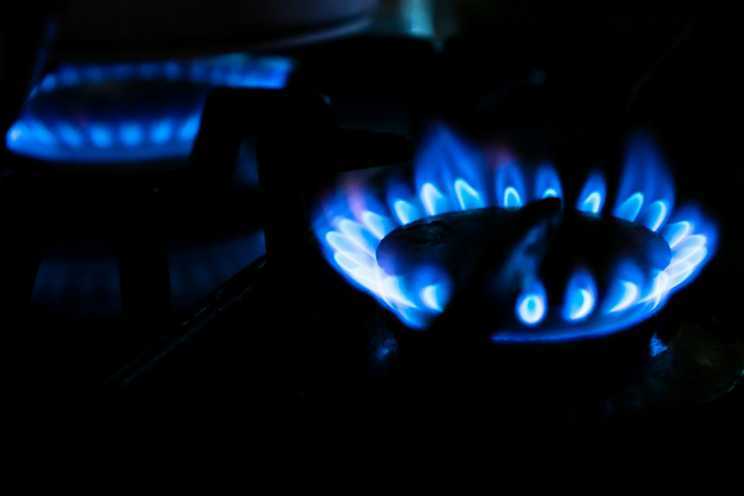 A close-up of a gas stove burner with blue flames in a dark environment.