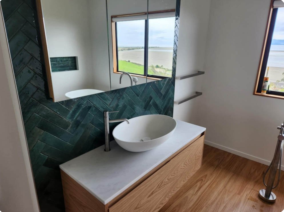 A modern bathroom with a vessel sink on a white countertop, a large mirror, and a window overlooking a green landscape with water.