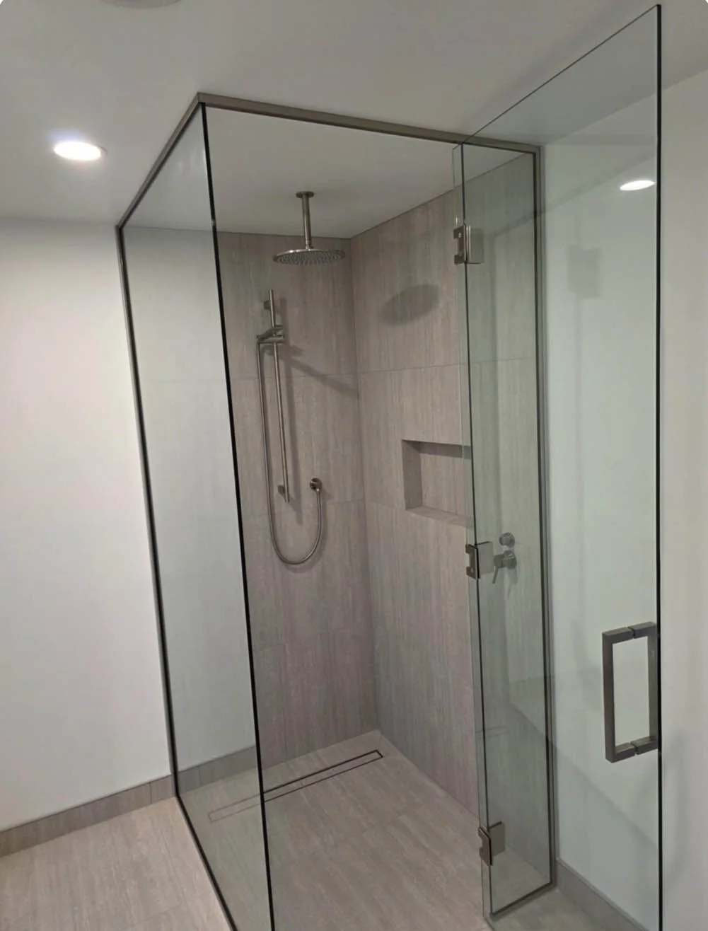 A modern walk-in shower with glass walls, a rainfall showerhead, a handheld shower, and a built-in niche for toiletries.