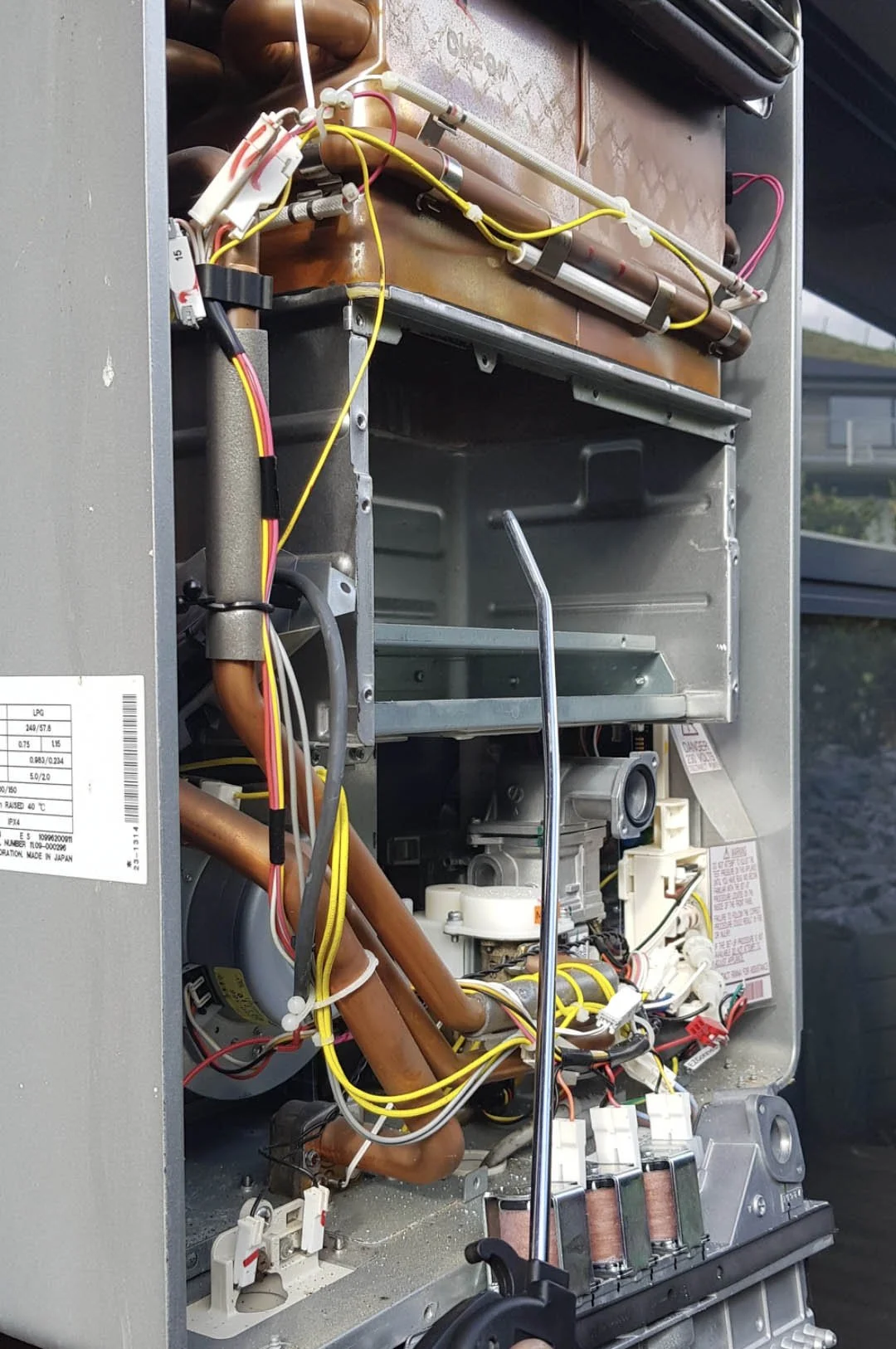 Open view of an HVAC or refrigerator unit showing internal components including wires, copper pipes, a fan motor, and other mechanical parts.