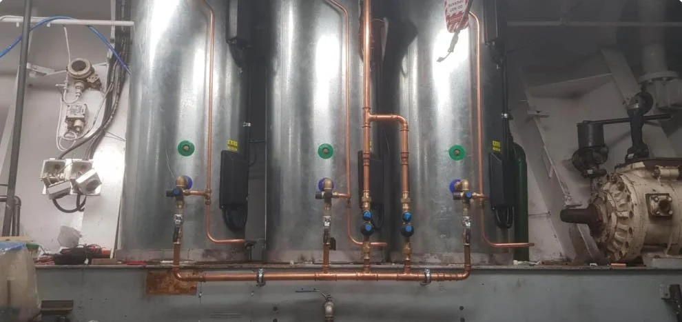 Three large metallic tanks with copper piping, valves, and fittings, part of an industrial setup or machinery, with electrical components nearby.