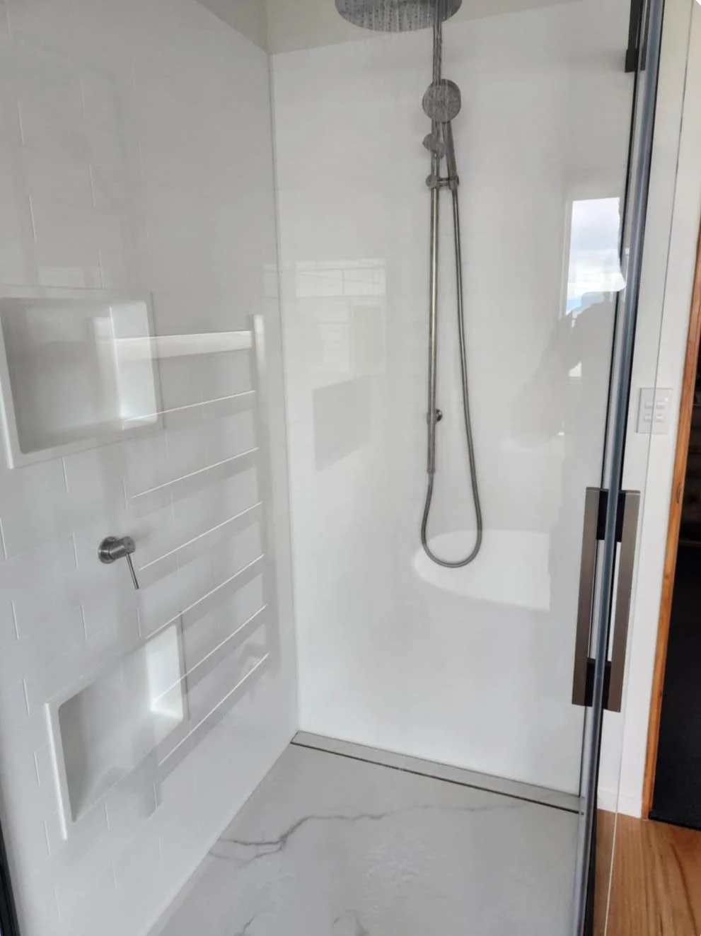 A modern walk-in shower with a clear glass door, featuring a rain showerhead and a handheld shower, white tiled walls, and a marble floor.