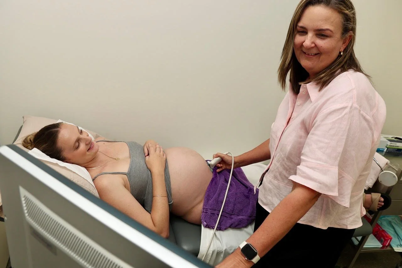 A pregnant woman lying in a hospital bed having an ultrasound performed by a healthcare professional.