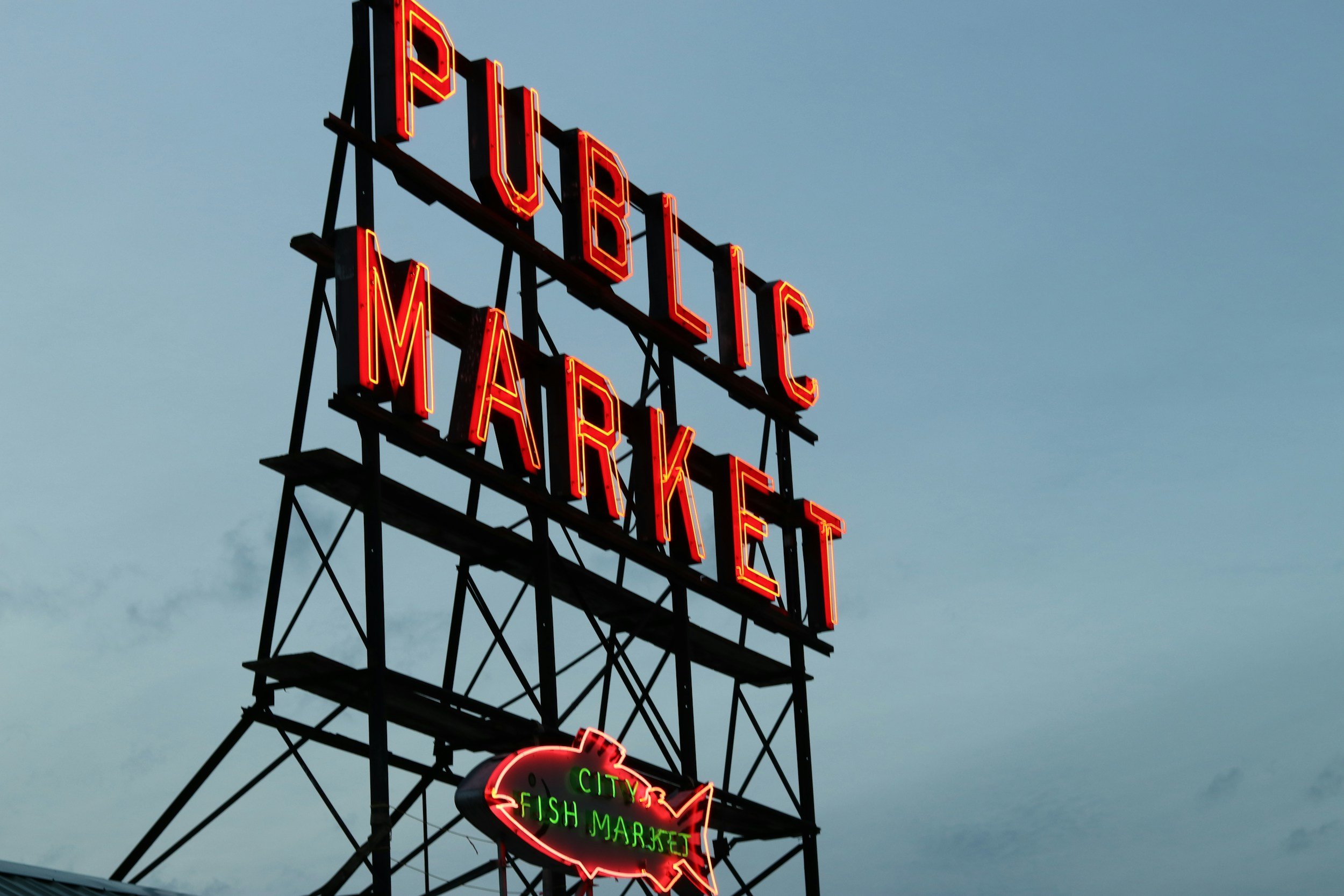 Neon sign for Public Market with additional sign below advertising City Fish Market, set against a cloudy evening sky.