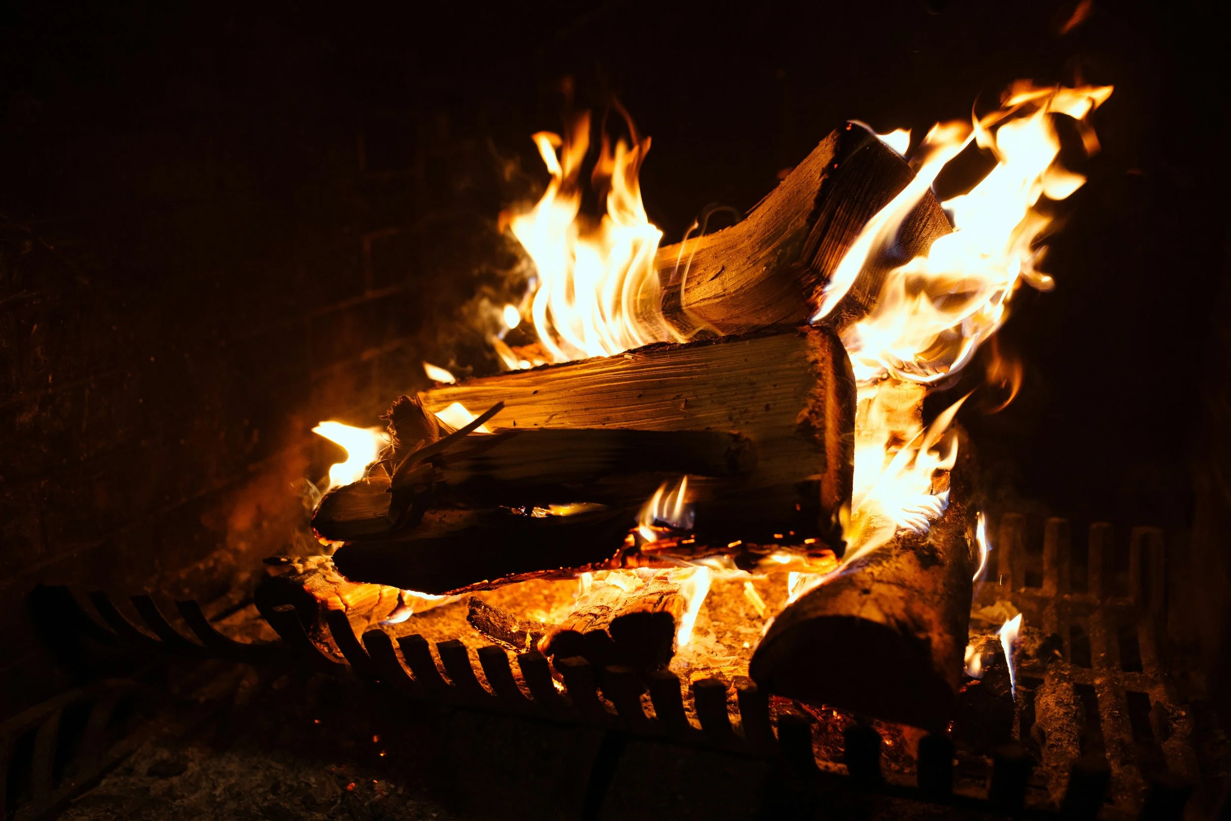 Fire burning logs on a grill in the dark.
