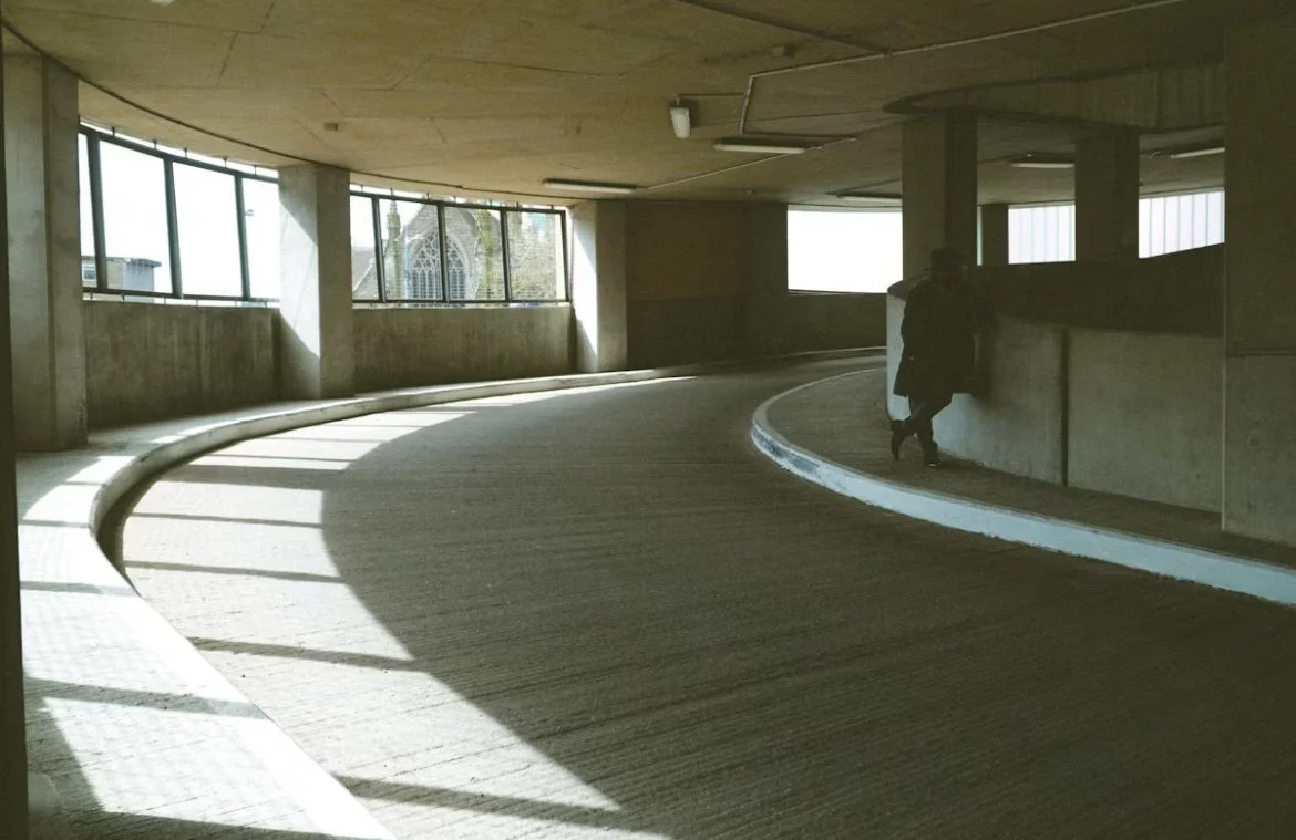 Interior view of a curved parking garage ramp with a person pushing a shopping cart.