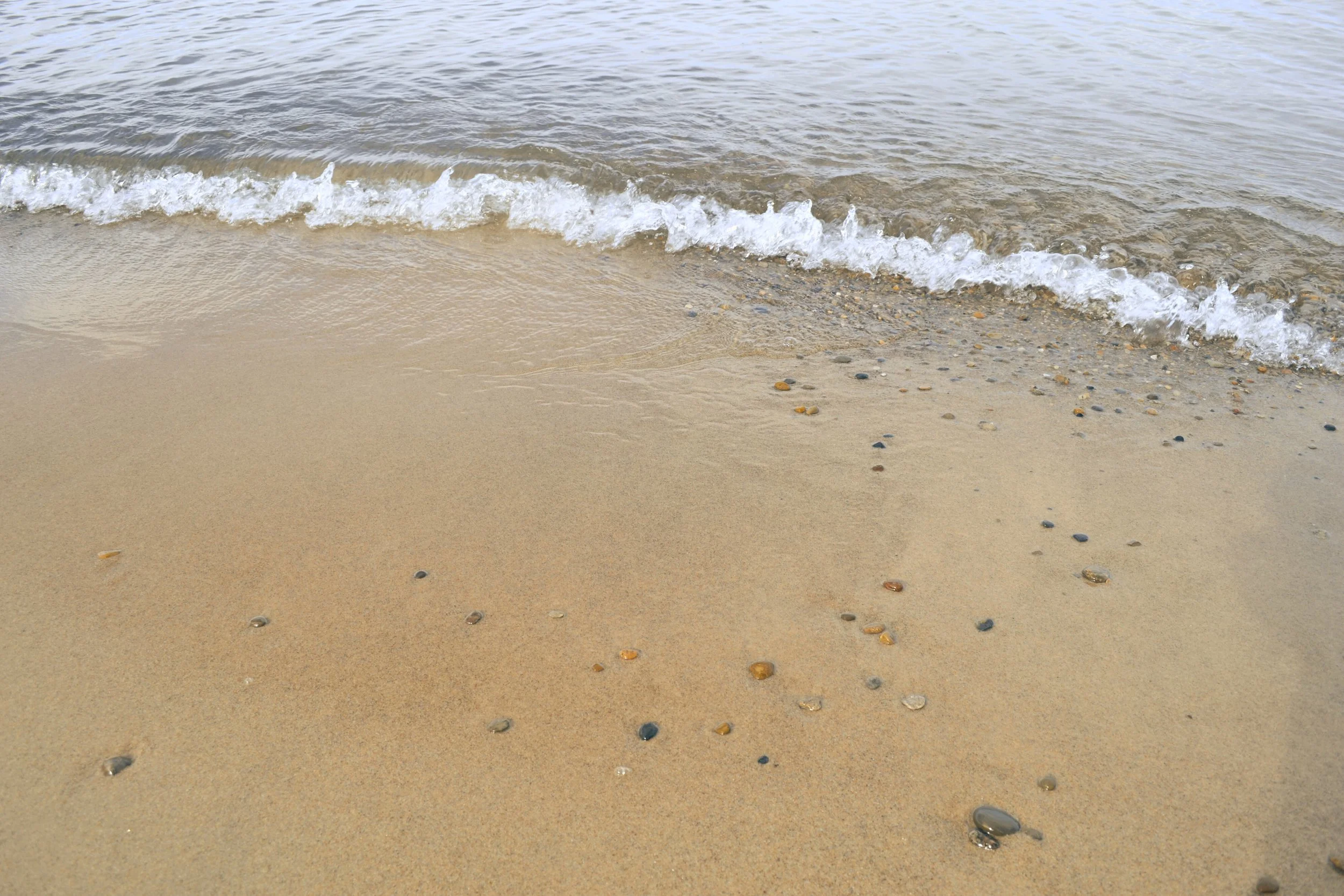 Gentle waves crashing on a pebbly beach to represent resilience and rhythm in deeper processing work which happens in therapy intensives offered by Adaptive Wellness