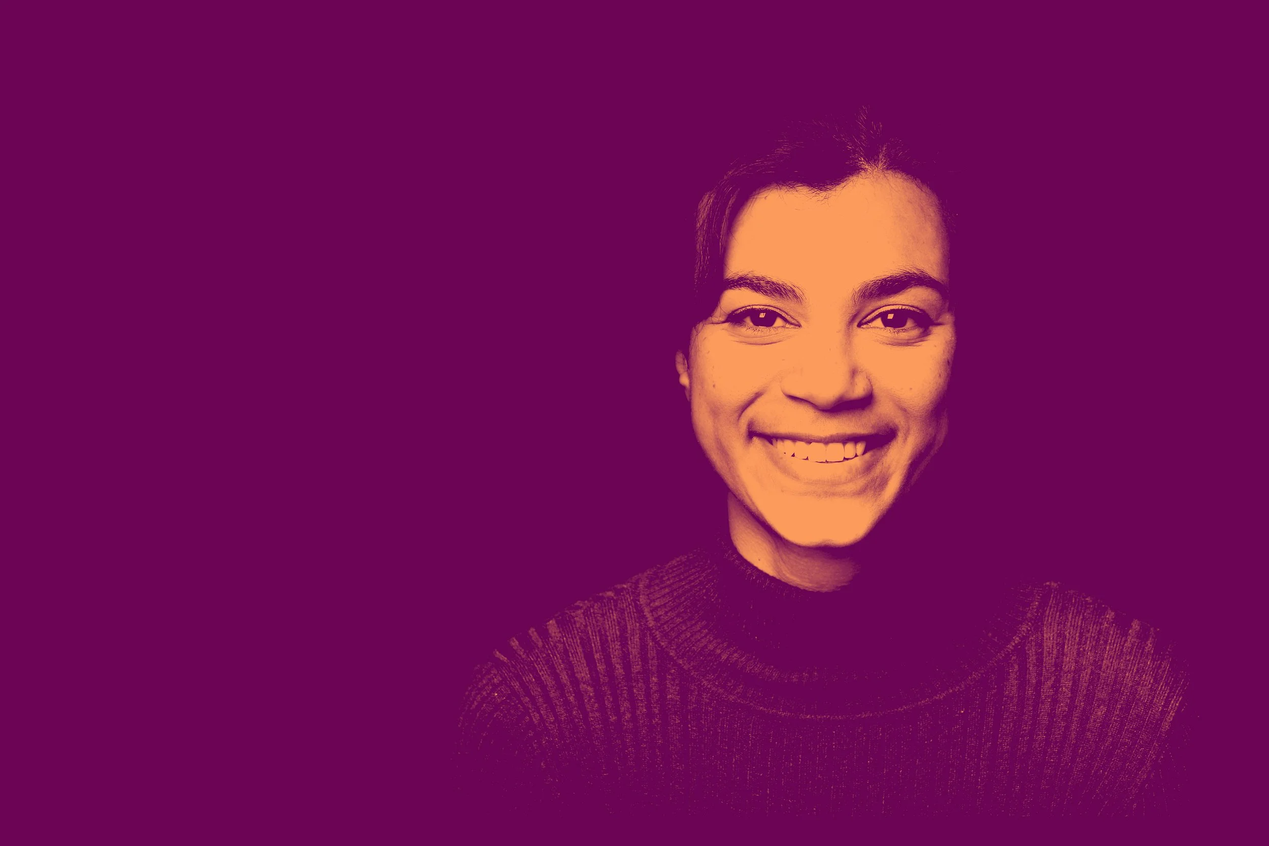 A woman with short dark hair, smiling, wearing a dark turtleneck sweater against a purple background.