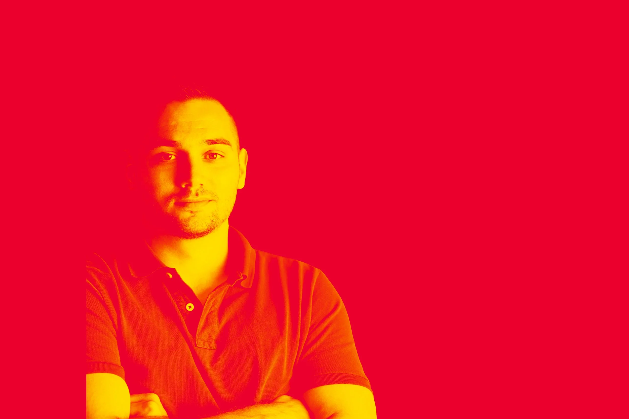 A man with arms crossed wearing a polo shirt, standing against a red background.