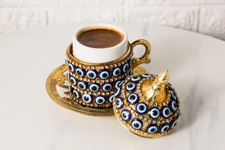 Turkish coffee served in a traditional evil eye patterned cup with a matching lid, placed on a decorative gold tray.