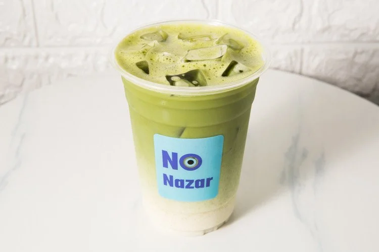 A plastic cup with green tea latte and ice cubes, labeled 'No Nazar'.