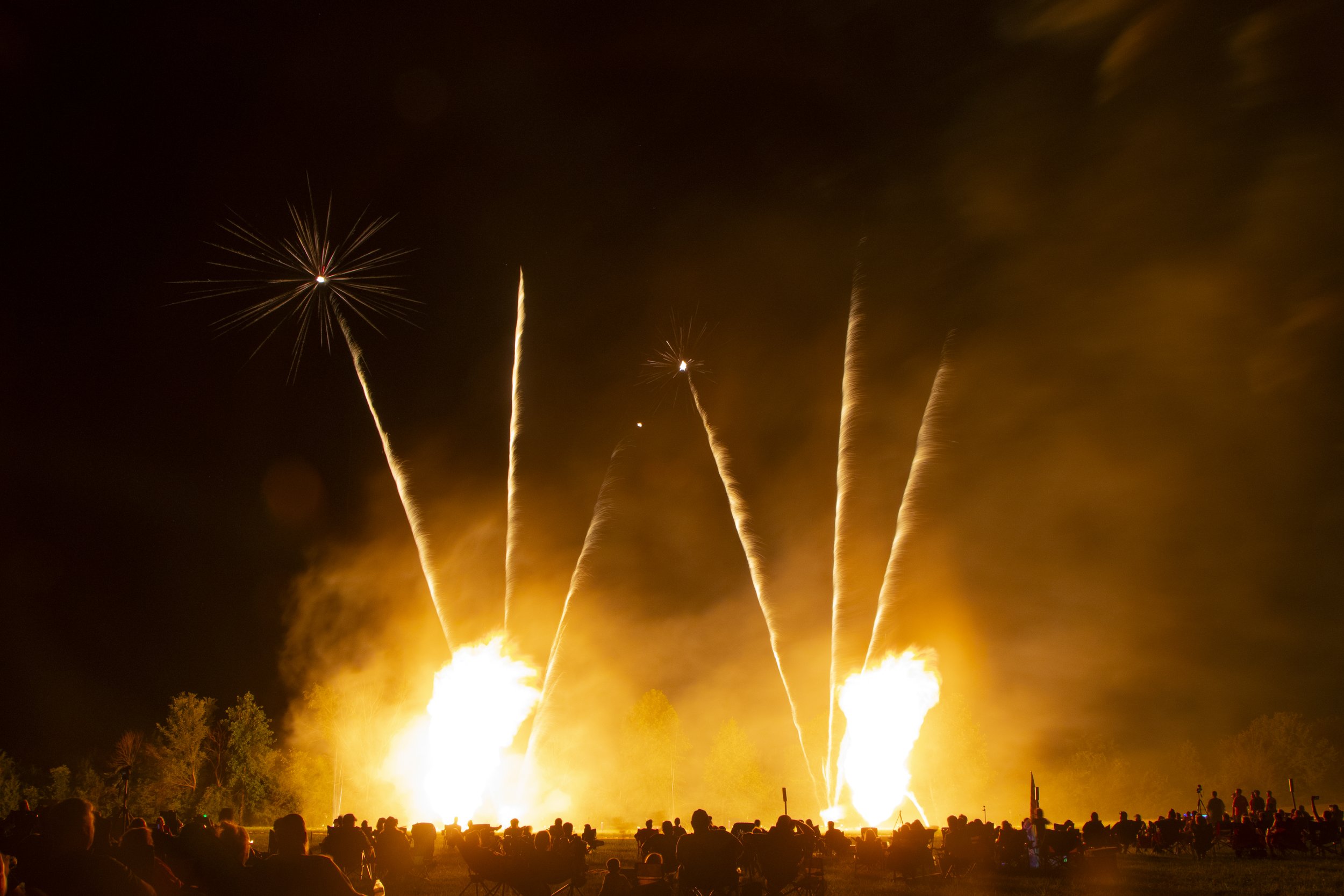 Fireworks and fireballs exploding in the night sky with a crowd watching from the ground at Fields of Freedom in Springfield, Missouri.