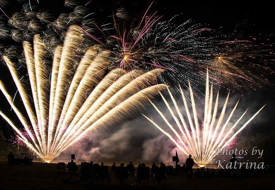 Fireworks display lighting up the night sky with colorful streaks and sparkles, with silhouettes of people watching.