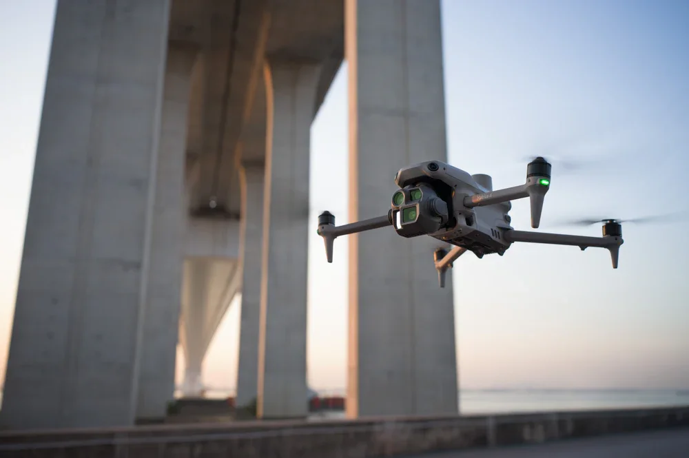A drone flying near large bridge supports at sunset.