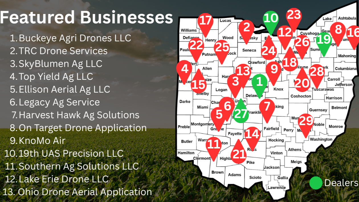 A gray pickup truck hauling a large outdoor mobile spray rig with a pink umbrella on top, in a green field near a cornfield, under a clear blue sky.
