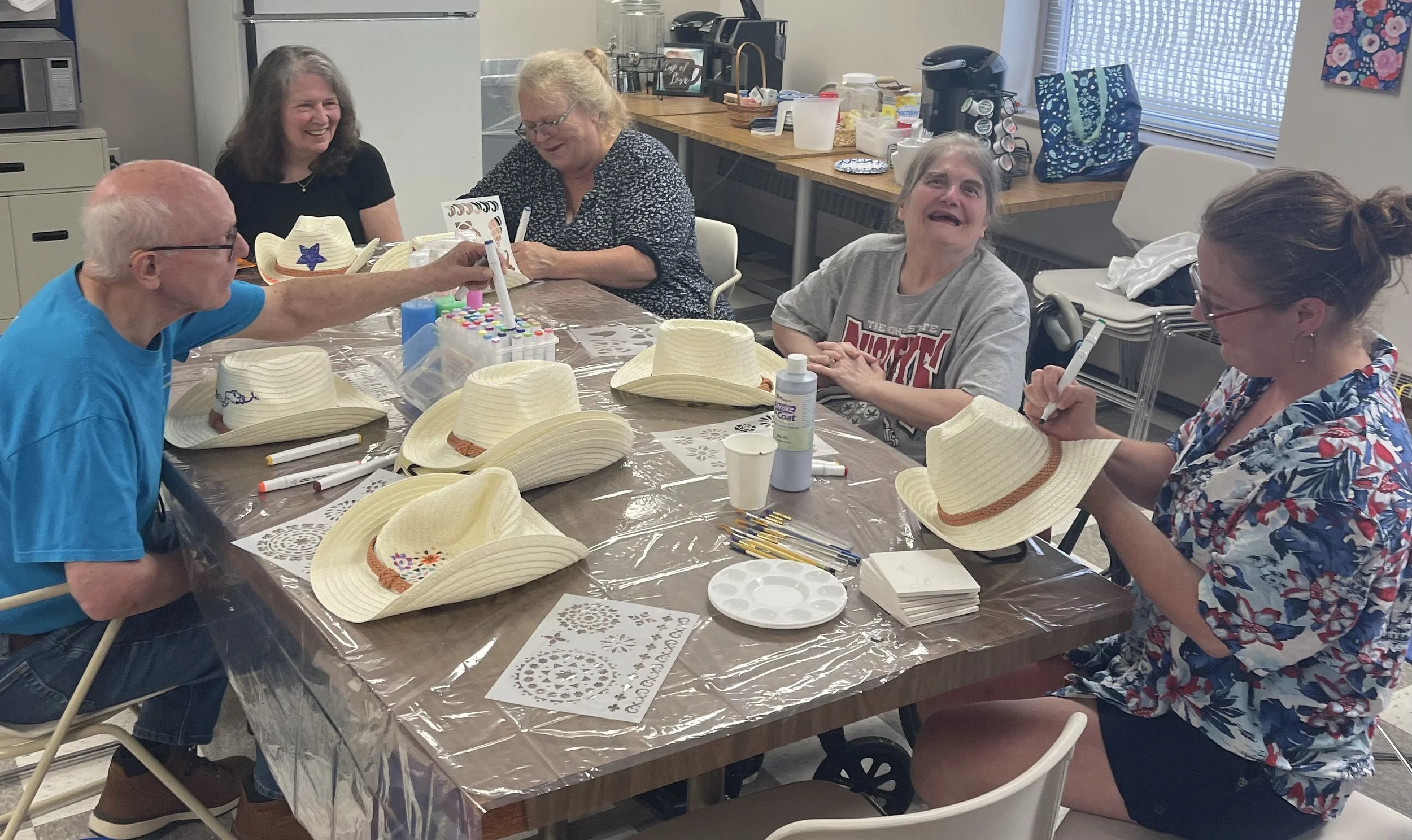 stroke survivors, caregivers, around a table with art therapist decorating cowboy hats