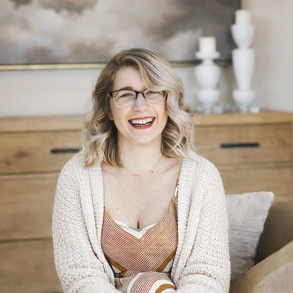 A woman with curly black hair and glasses smiling at the camera.