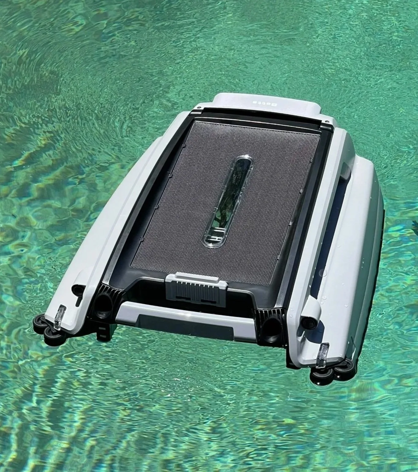 A robotic pool cleaner floating on the surface of a swimming pool with clear green water.