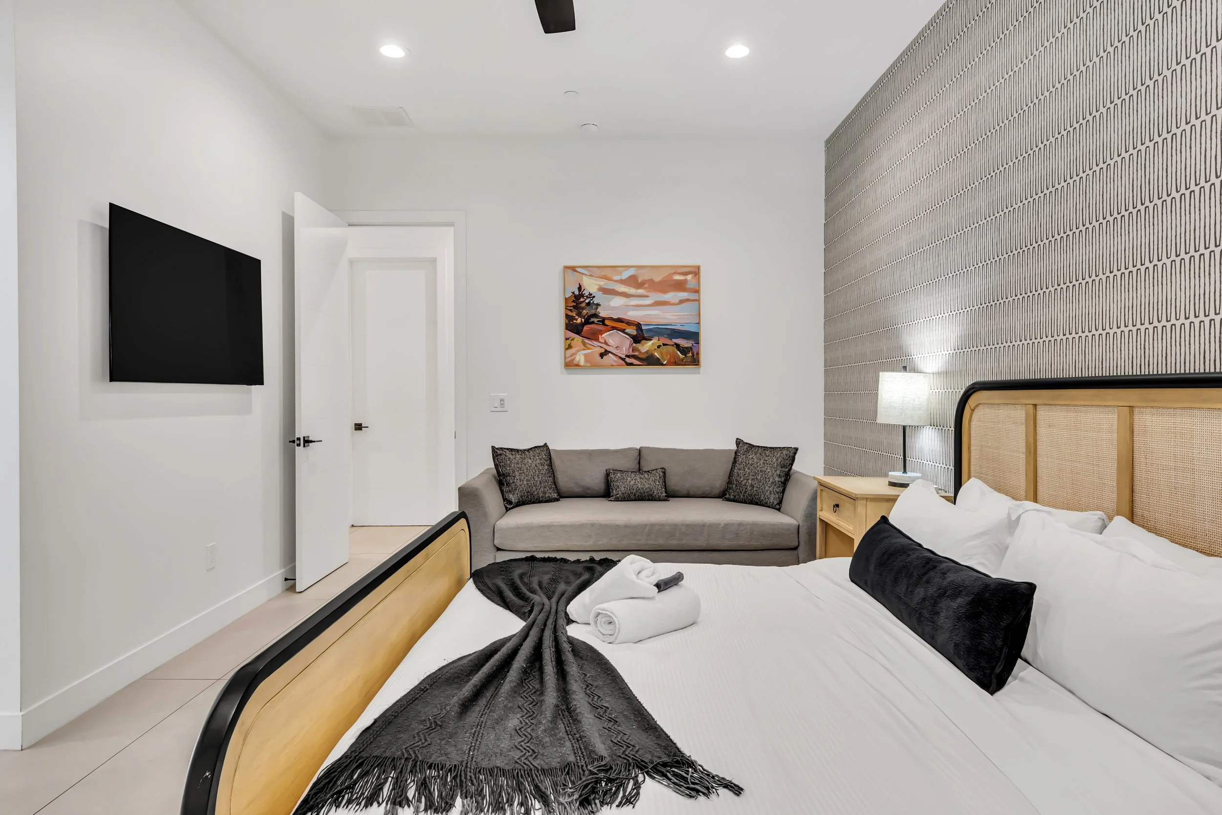 Bright bedroom with a seating area, patterned accent wall, mounted TV, and warm layered bedding in Scottsdale, Arizona.