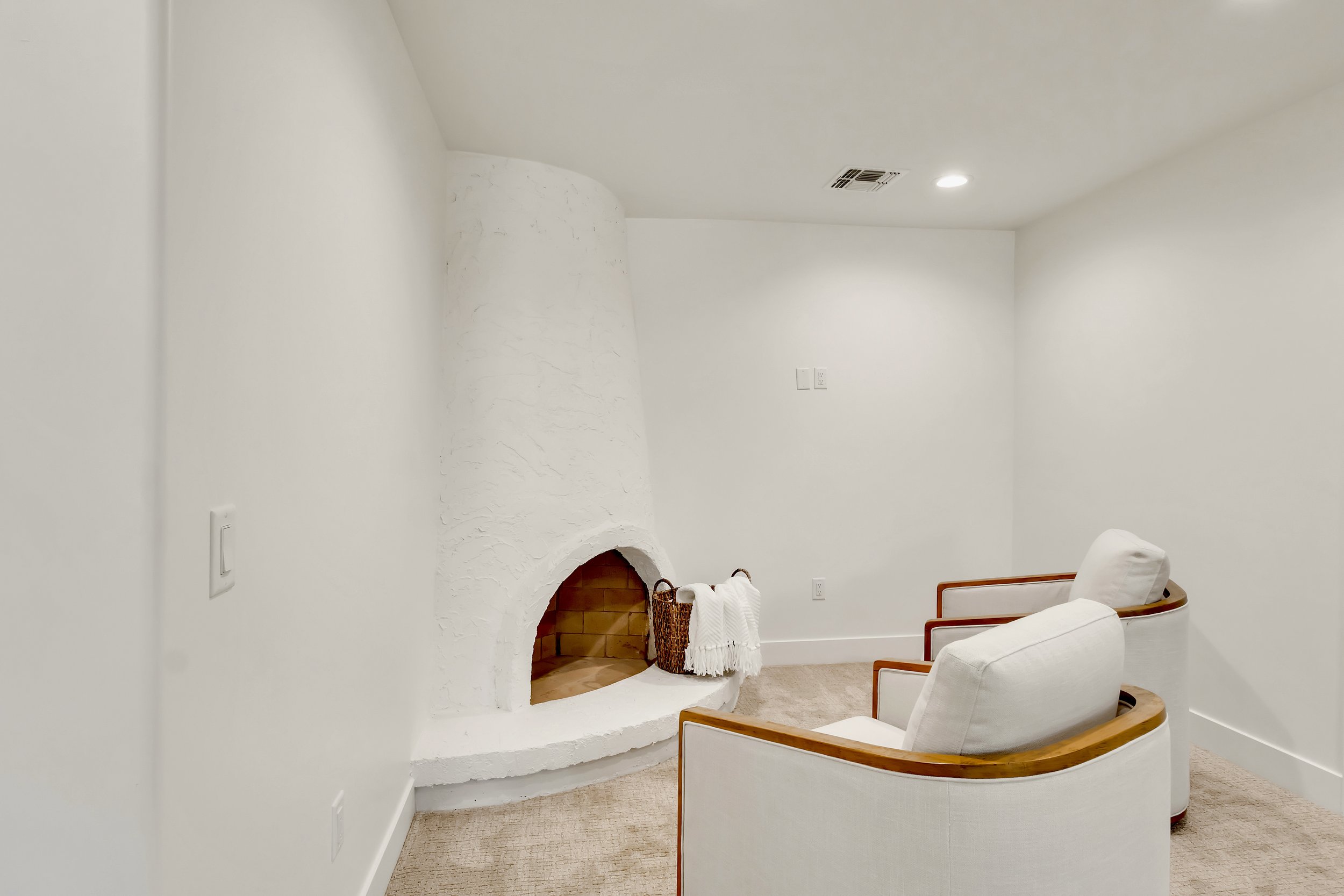 Cozy sitting area in Phoenix, AZ featuring a white kiva-style fireplace and upholstered modern armchairs.