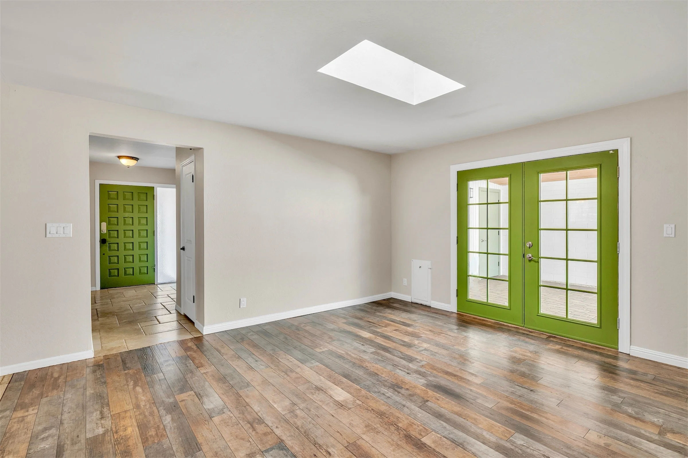 Bright empty living space with green doors and skylight in Tempe, AZ, captured with professional real estate photography highlighting natural light and modern flooring.