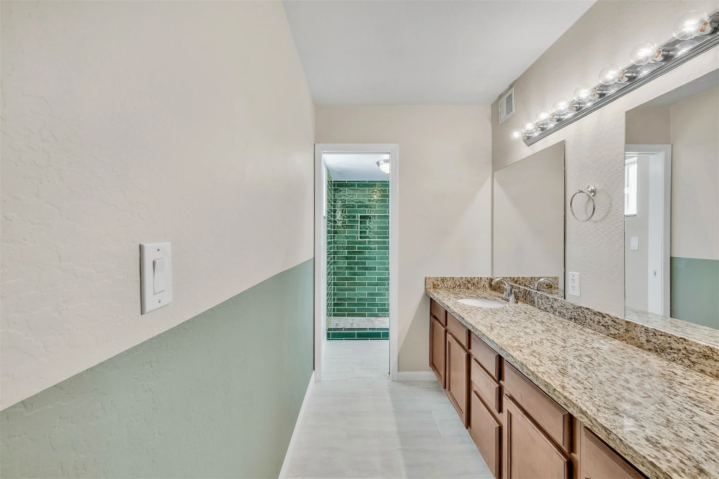 This bathroom in Tempe, AZ features a granite countertop, green tiled shower, and modern fixtures, captured perfectly for real estate photography.