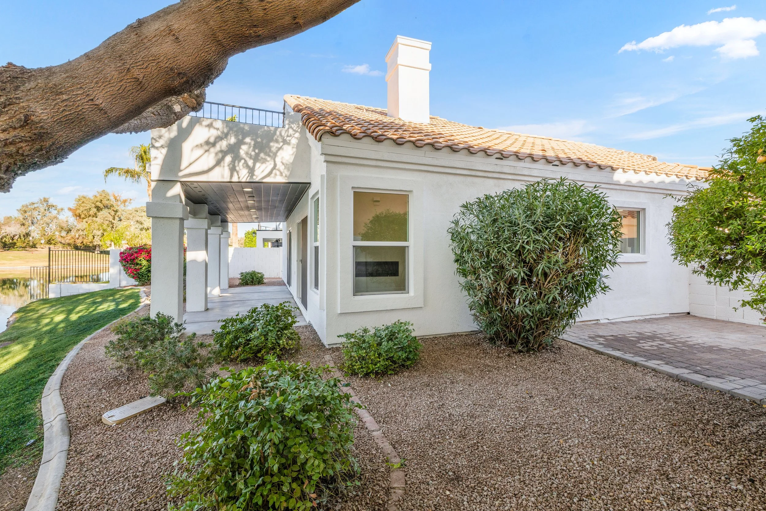 This real estate photography showcases a beautiful lakefront house with a tiled roof and lush garden in Chandler, AZ, highlighting its serene outdoor living spaces and stunning views.