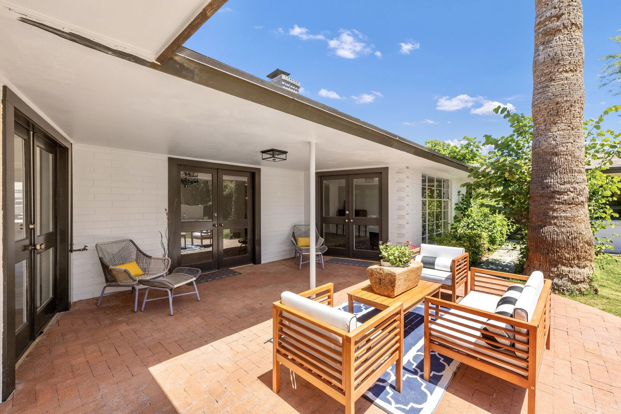 Beautiful covered patio with wooden furniture and brick floor in Phoenix, AZ, captured with professional real estate photography to showcase outdoor living space.