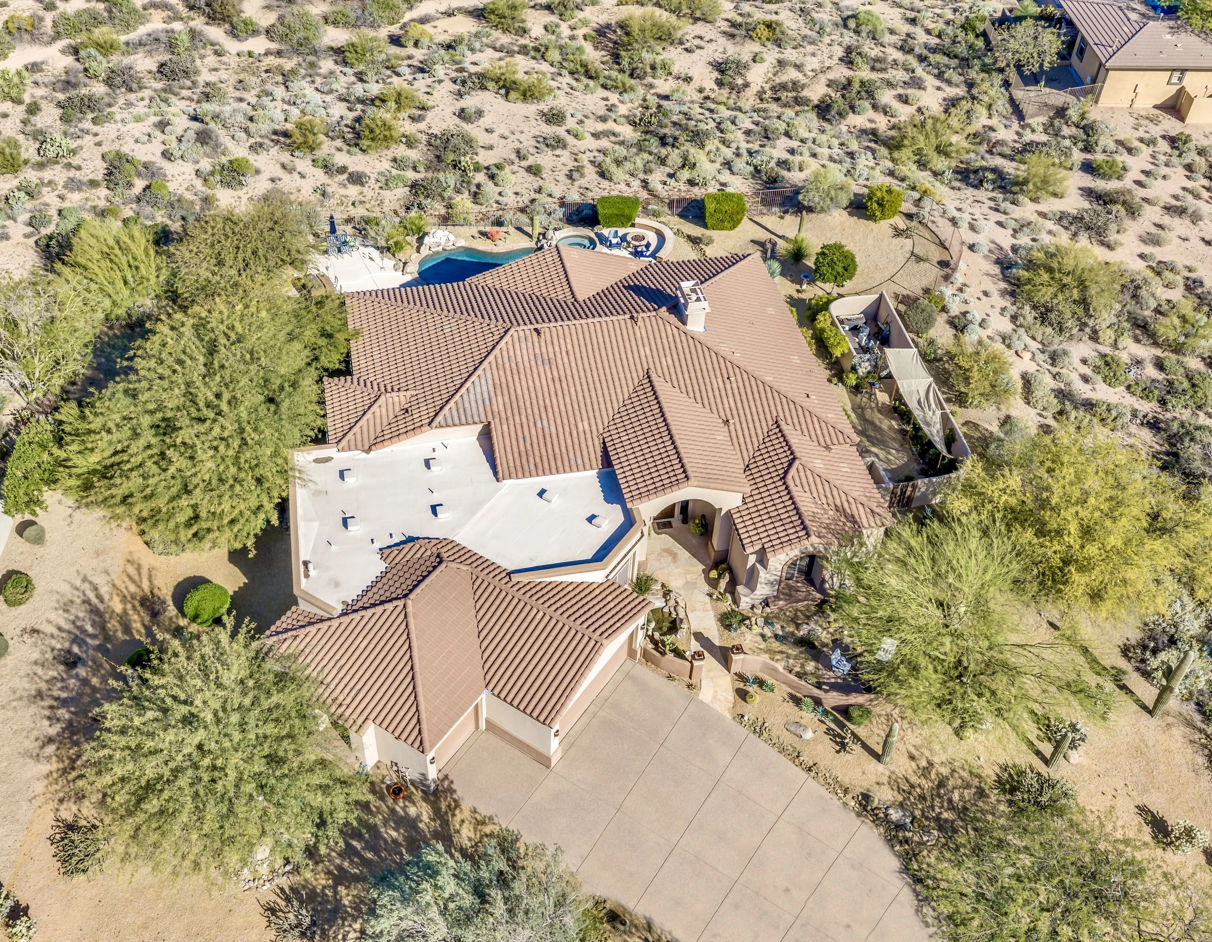 This aerial real estate photography showcases a beautiful desert home with a pool and spacious backyard in Scottsdale, AZ, highlighting its unique Southwestern architecture and natural landscape.