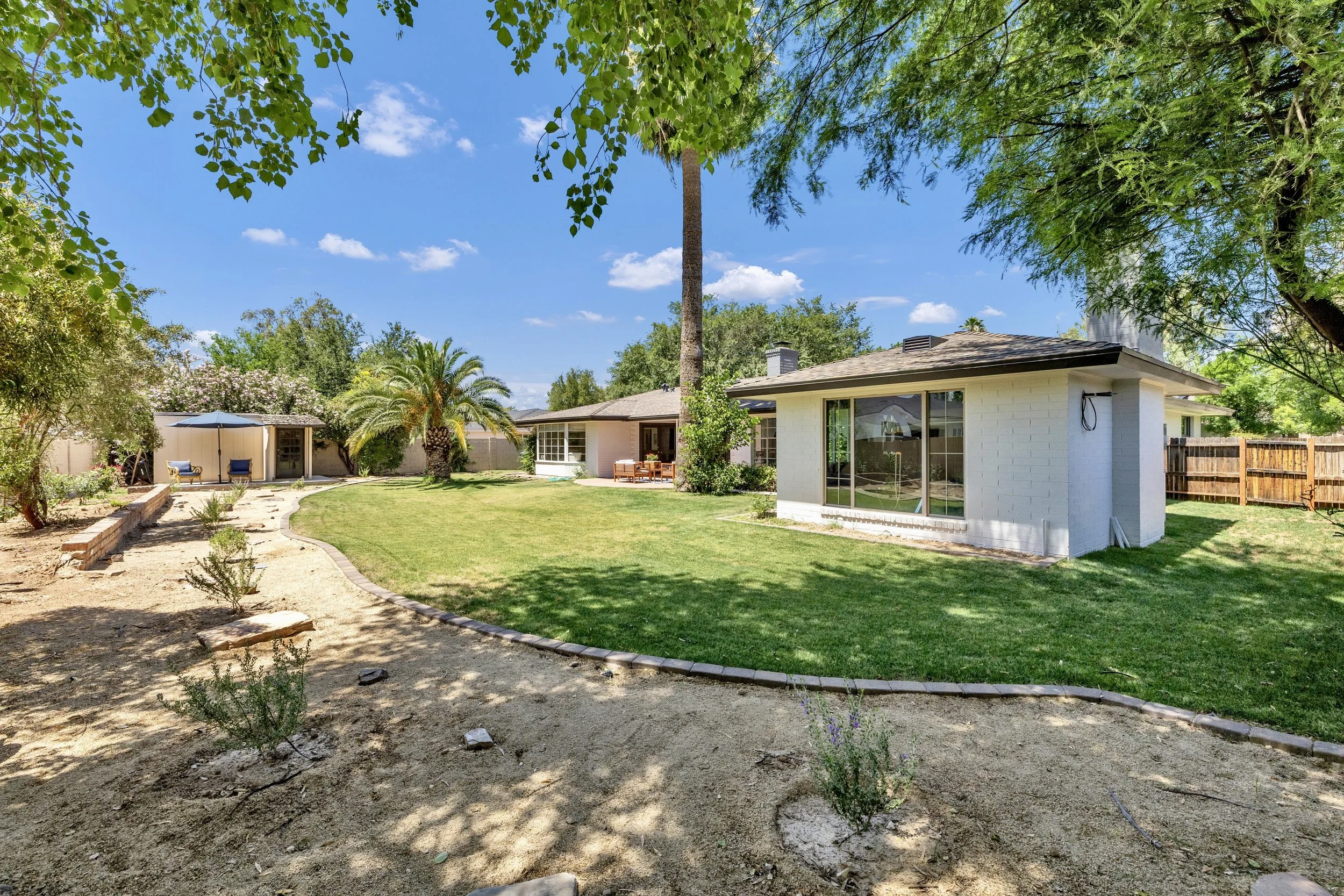 This Phoenix, AZ backyard features a spacious green lawn, mature trees, and a relaxing outdoor seating area captured with expert real estate photography.