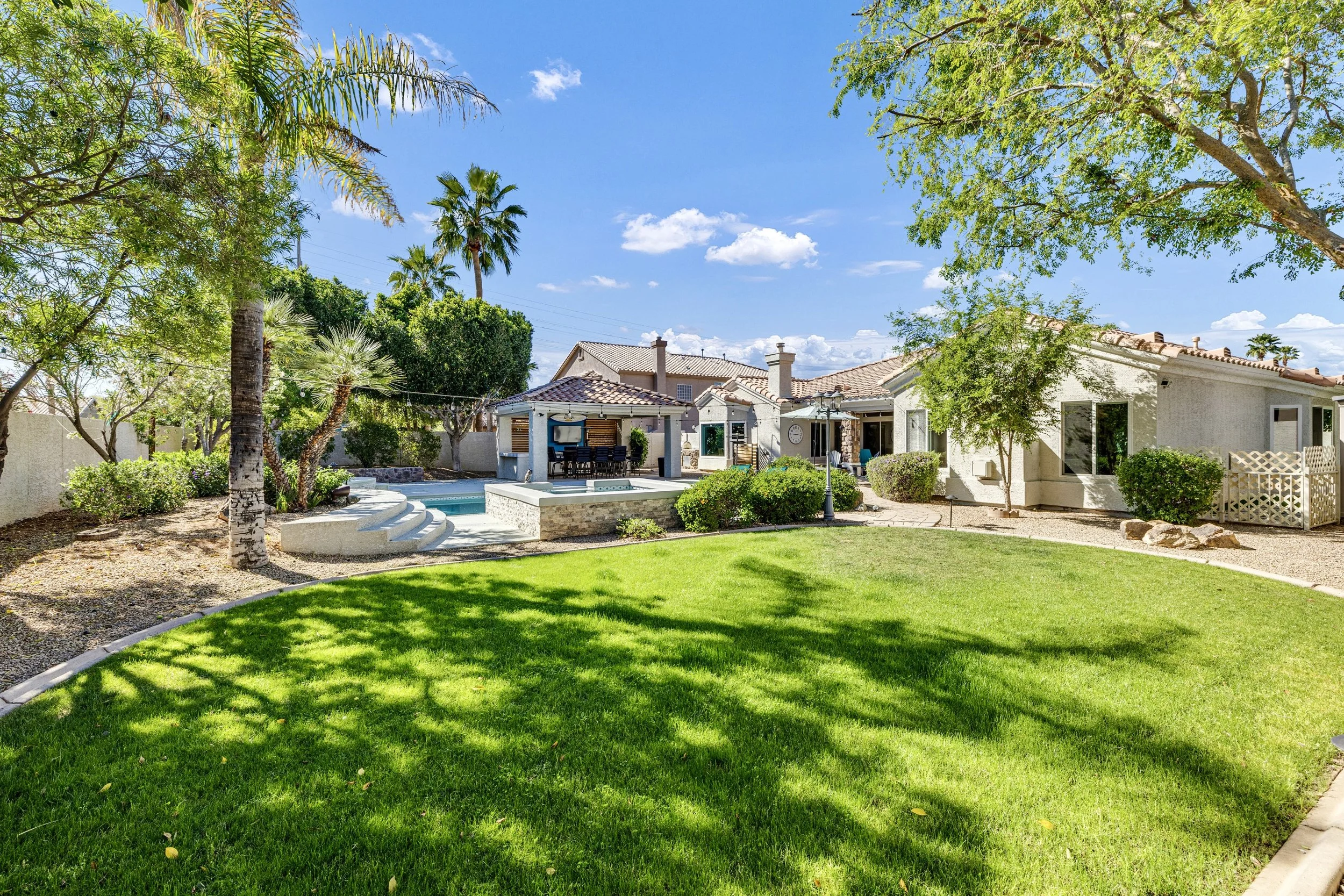 This Gilbert, AZ backyard features a beautiful pool, covered patio, and lush lawn, captured with professional real estate photography to showcase the home's inviting outdoor space.