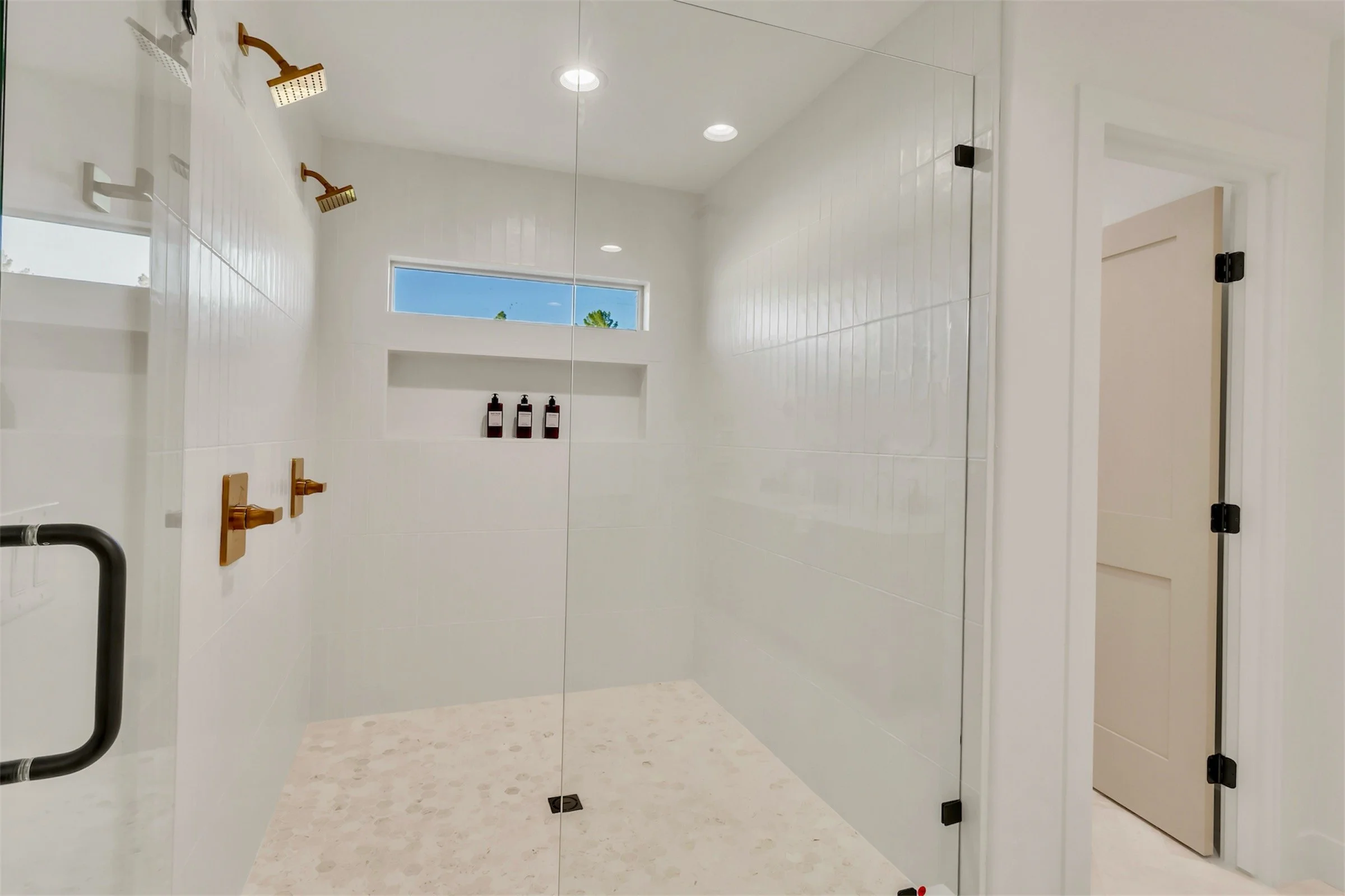 Spacious walk-in shower with dual gold fixtures and white tile walls in a modern Phoenix, AZ bathroom.