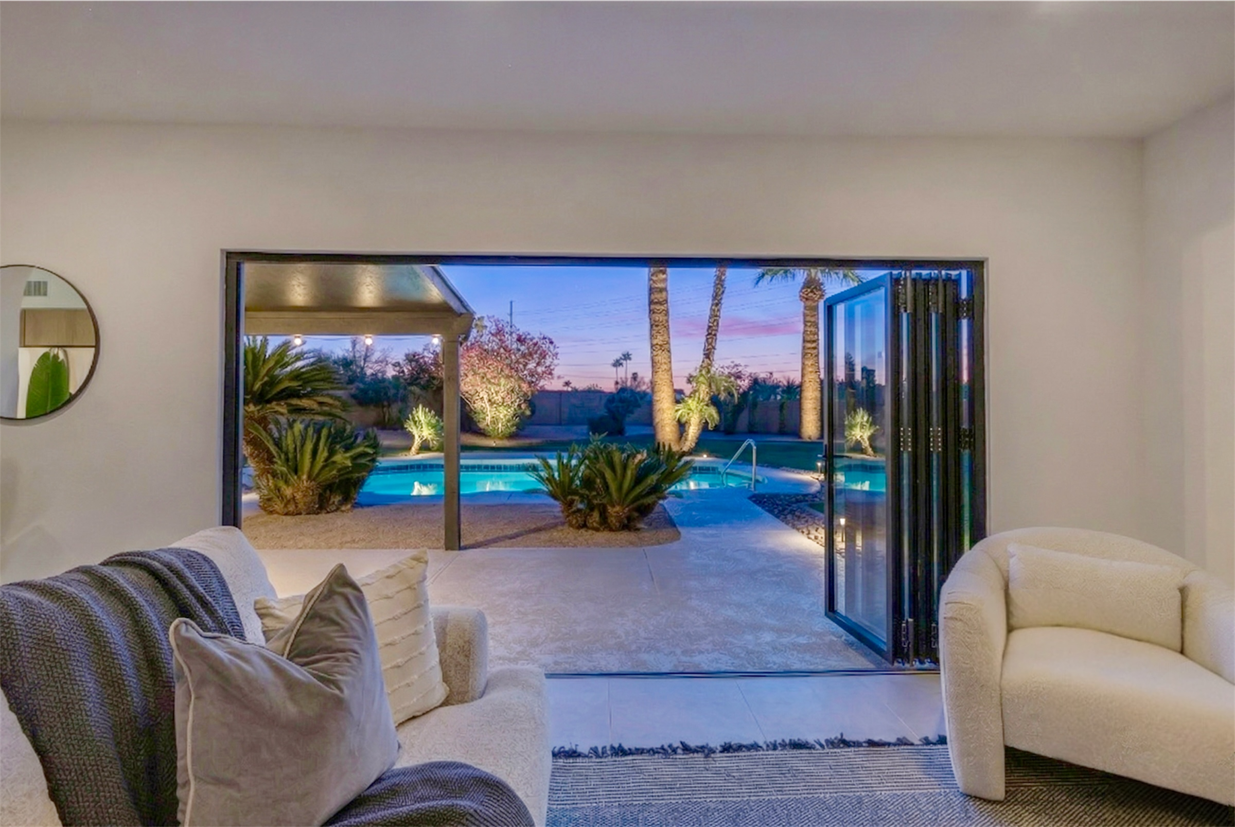 This Scottsdale, AZ living room features a modern design with an open view of a beautifully lit backyard pool, showcasing excellent real estate photography.