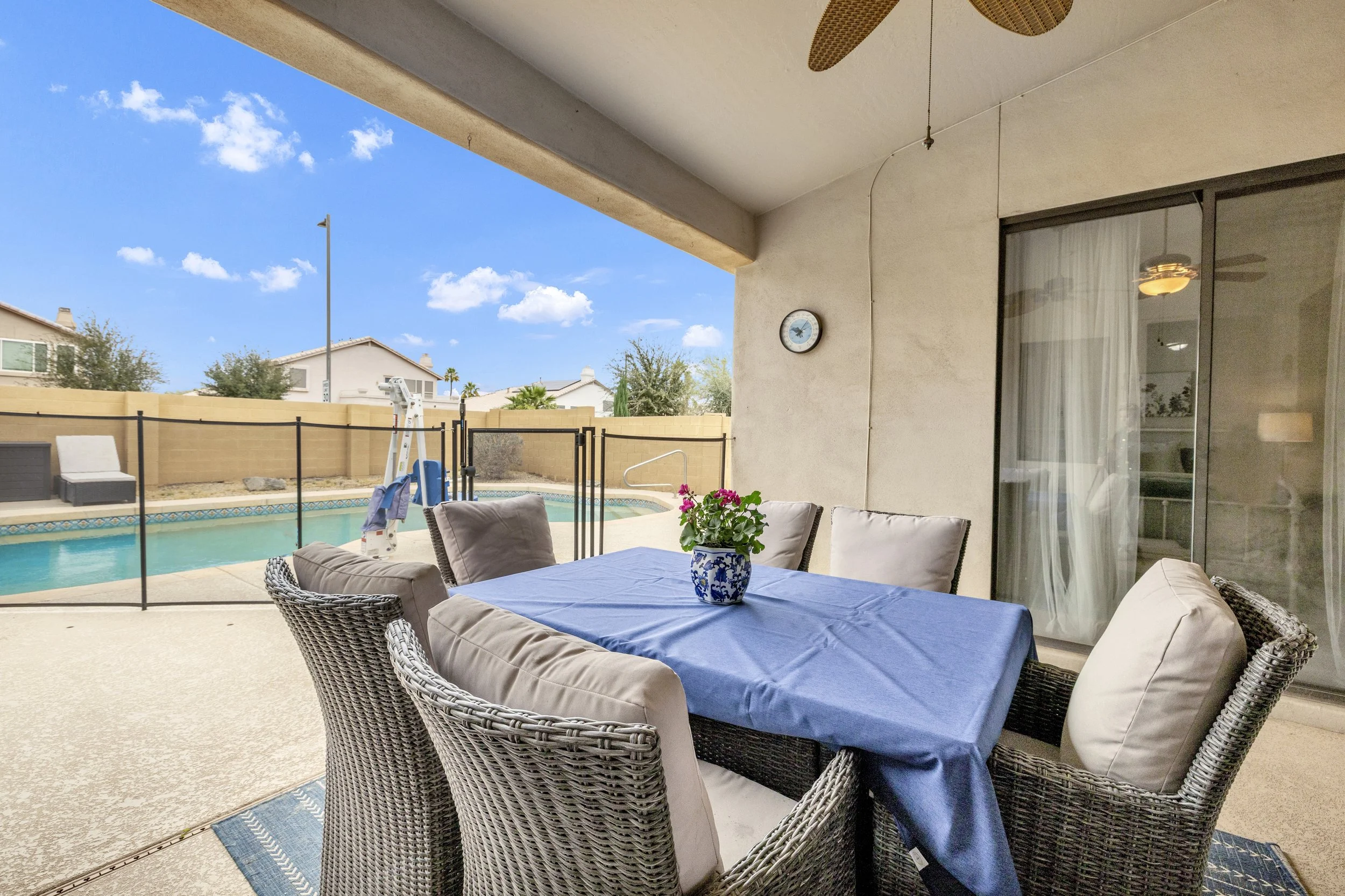 This covered patio dining area overlooks a fenced pool in Goodyear, AZ, showcasing excellent real estate photography for outdoor living spaces.