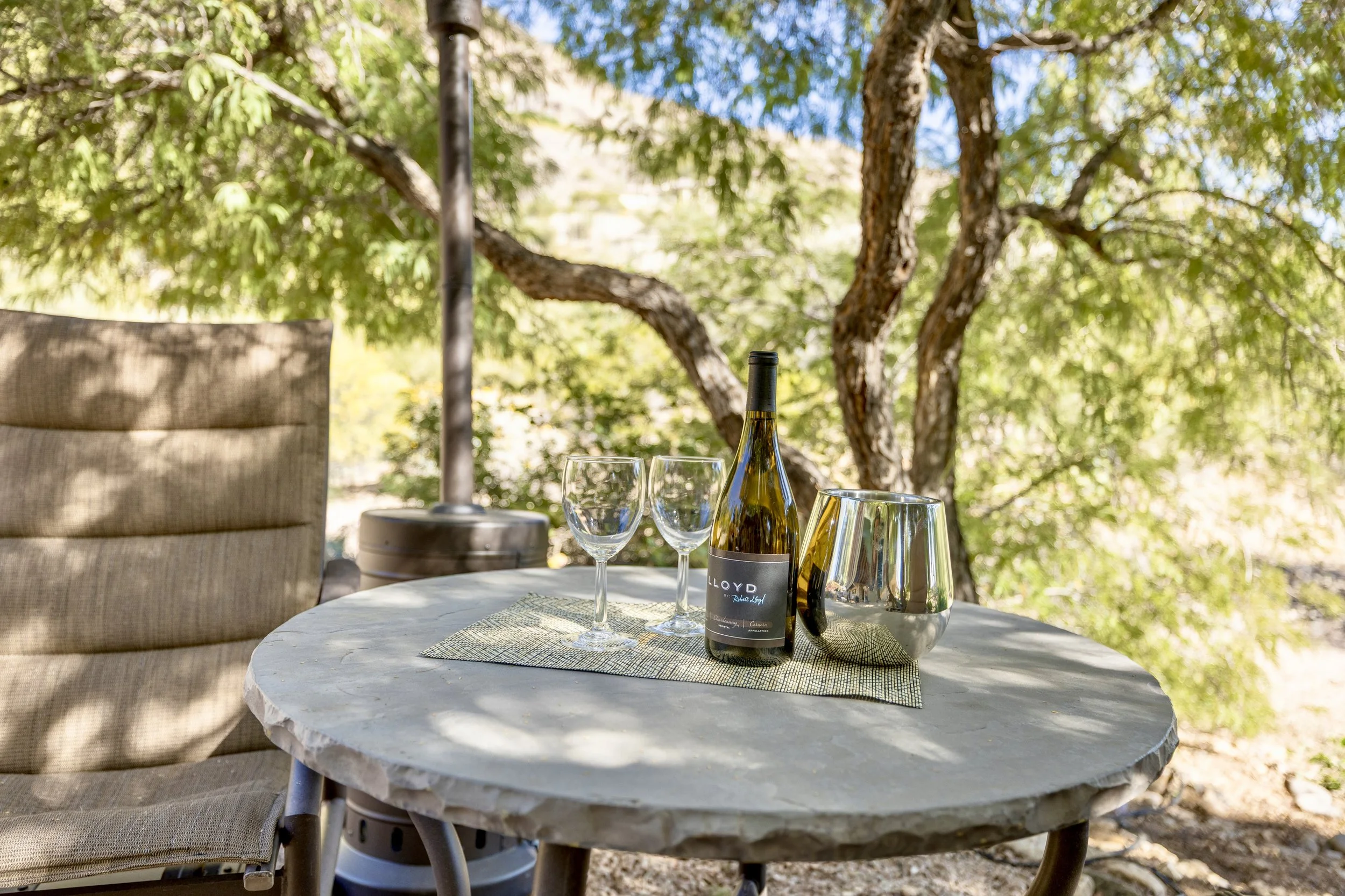 This shaded outdoor patio in Paradise Valley, AZ features a stone table set with a wine bottle and glasses, captured beautifully through real estate photography for a serene ambiance.