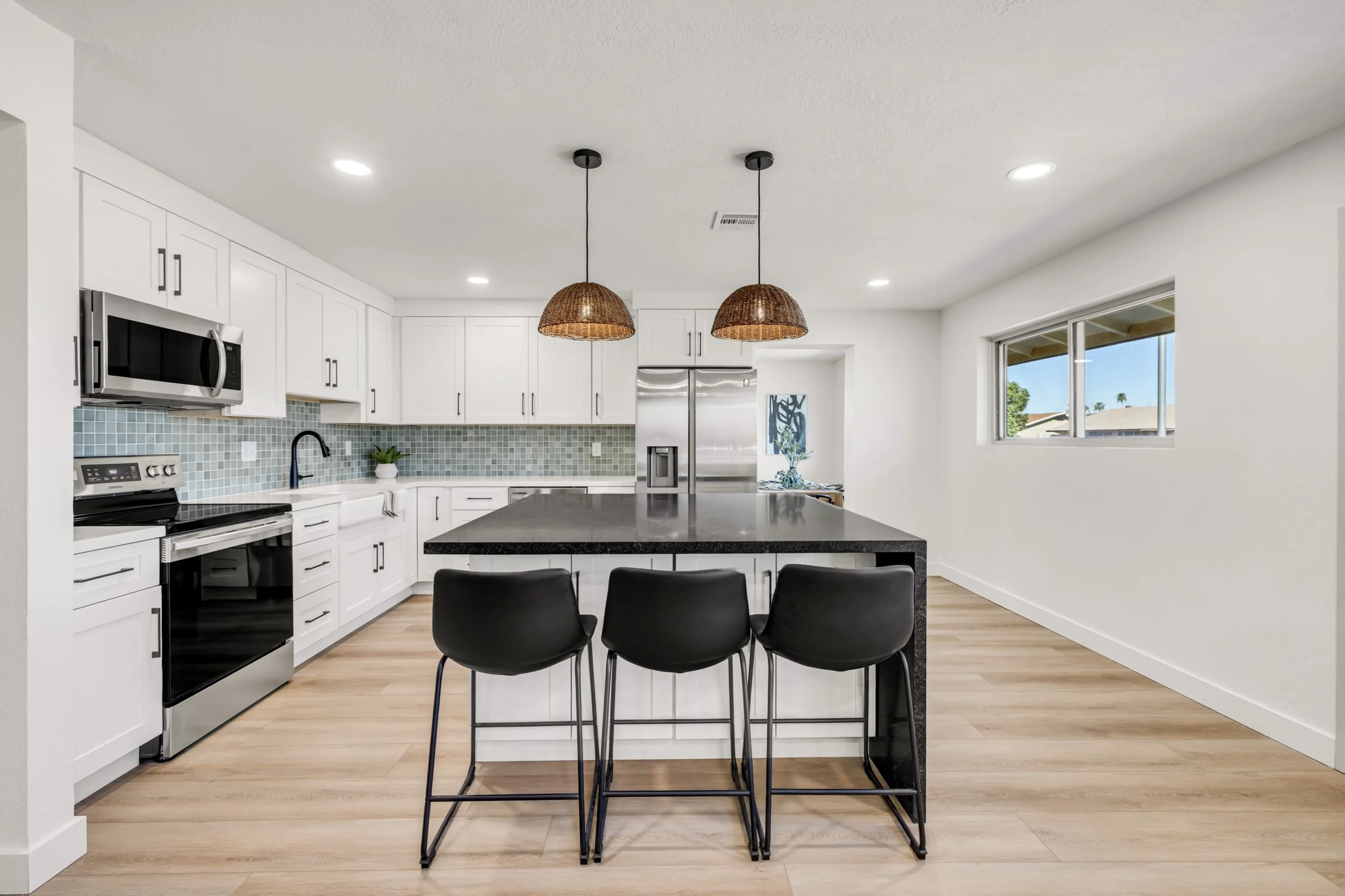 This modern kitchen in Mesa, AZ features a spacious island with black countertops, three barstools, and stylish pendant lighting, captured with expert real estate photography.