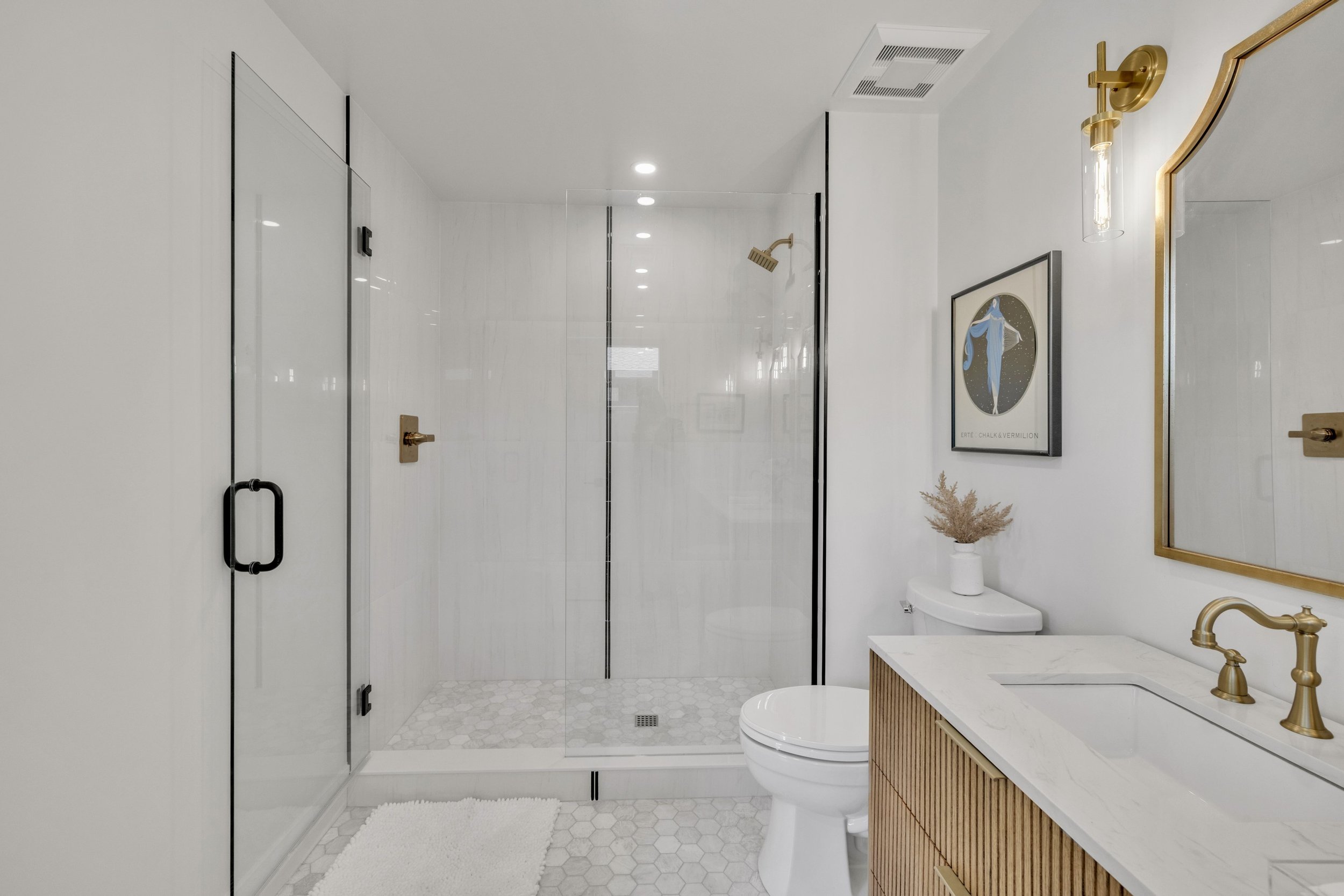 This modern bathroom in Phoenix, AZ features a glass shower, wooden vanity with gold fixtures, and elegant decor, perfectly captured through expert real estate photography.