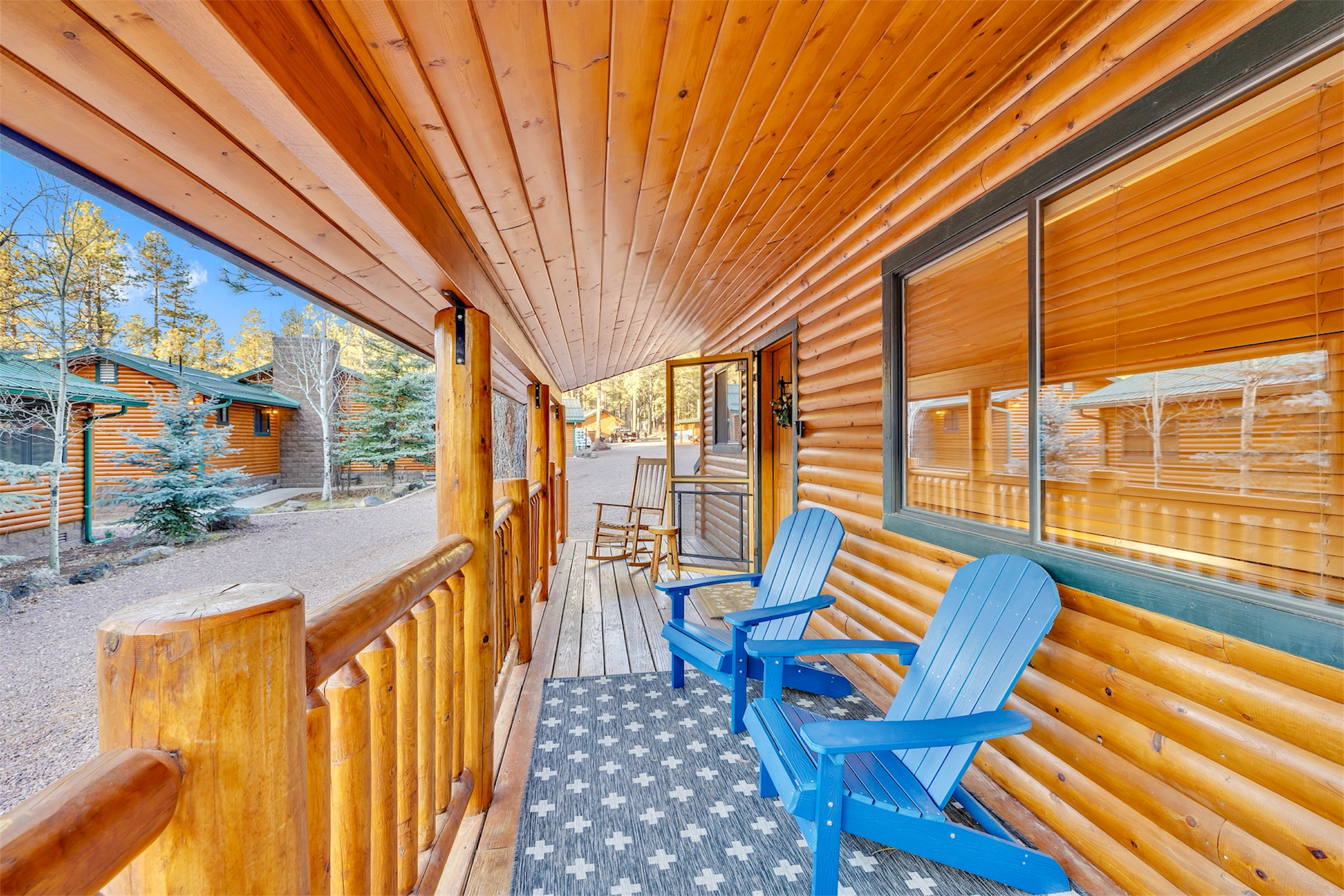 Cozy log cabin porch in Greer, AZ featuring blue Adirondack chairs and wooden railing captured with professional real estate photography showcasing rustic charm.