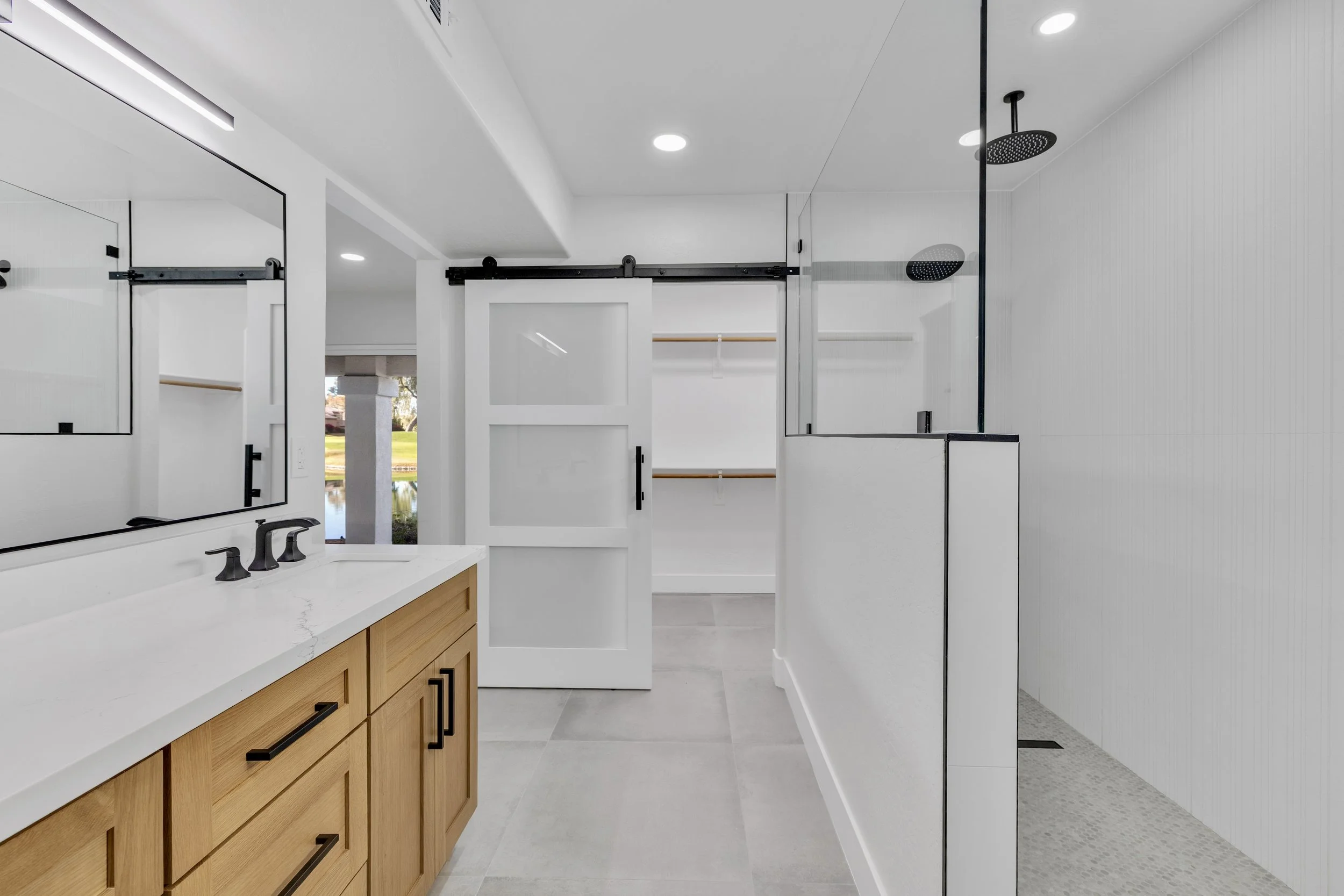 This modern bathroom in Chandler, AZ features sleek fixtures, a spacious walk-in shower, and a wooden vanity, perfectly showcased through professional real estate photography.